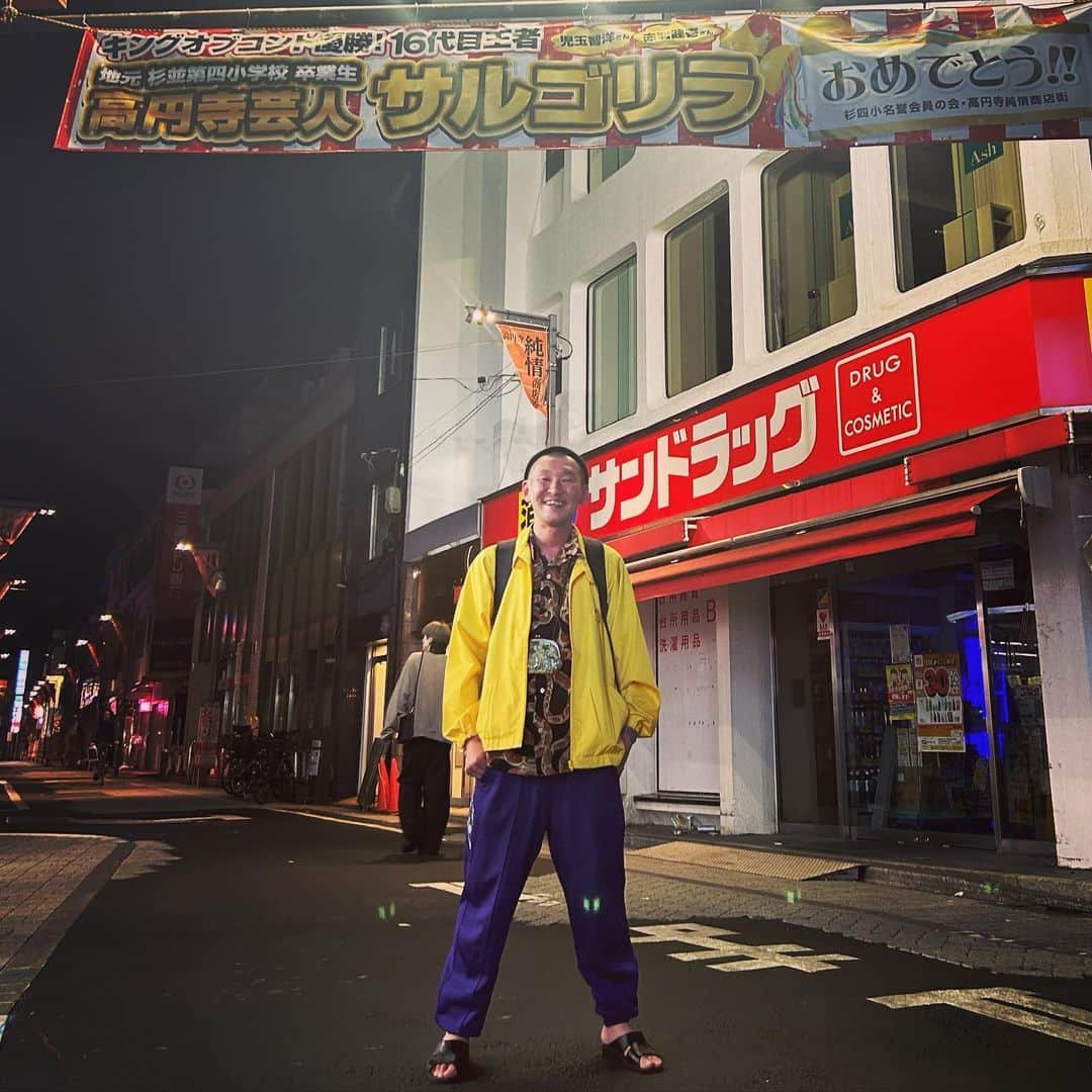 のインスタグラム：「今日の服装。 渋谷でライブとサルゴリラ赤羽さん祝いの会の日。  かたつむりピーチさんに先日頂いた蛇のシャツに十四才のジャケット。 スーパースターのジャージ。 ROTOTOのニット帽に黒の便所サンダルで金のがま口にmont-bellのメッシュリュック。  新ネタライブねたログを終えたあと高円寺でサルゴリラ赤羽さんのキングオブコント優勝祝勝会をして赤羽さんと純情商店街のサルゴリラさん優勝横断幕の前で赤羽さんに撮って頂きました。 僕も頑張ろう。 赤羽さんありがとうございます。 優勝おめでとうございます。  #今日着た服 #ファッション #古着 #高円寺 #サルゴリラ #優勝 #赤羽さんお洒落 #衣と食とKEN」