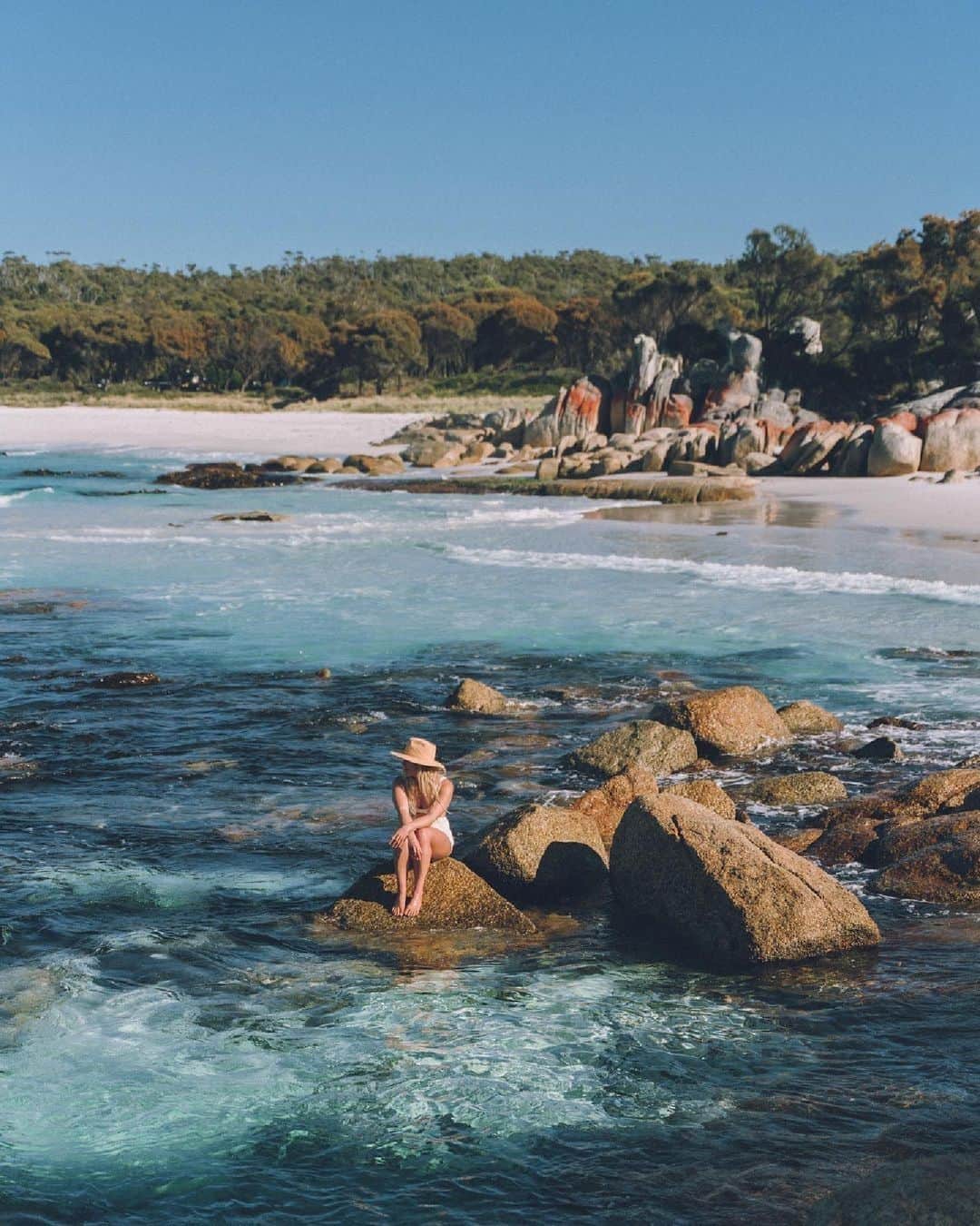 Australiaのインスタグラム：「The Bay of Fires looking ~ fire ~ as per usual 🔥💙 We're loving this Mamma Mia moment from @kendallbaggerly in the clear blue waters of larapuna (#BayOfFires). This vibrant spot on the nipaluna (@tasmania) coast is best known for its orange lichen-covered rocks, but its string of bays is also home to postcard-worthy hiking trails, colourful reefs and diverse birdlife 🦜. Immerse yourself in the wilderness of @eastcoasttasmania during a four-day expedition with @taswalkingco, or plan your own adventure with nights spent beneath the trees at @bayoffiresbushretreat ⛺   #SeeAustralia #ComeAndSayGday #DiscoverTasmania #EastCoastTasmania  ID: A woman in a hat and swimwear sits on a rock, surrounded by clear, blue water. The white sandy beach is in the background, with orange tinged rocks and greenery dotting the coastline.」