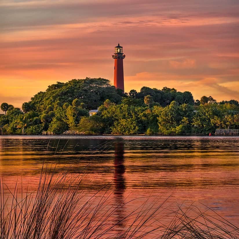 アメリカ内務省のインスタグラム：「The 120-acre Jupiter Inlet Lighthouse Outstanding Natural Area offers a break from the hustle and bustle of Florida’s urbanized Treasure Coast. Take a gentle walk along a trail or boardwalk through native and restored coastal habitat.    The area is home to a remarkable array of natural and cultural resources, including four sensitive habitats, 26 special status species and evidence of human activity dating back over 5,000 years.    Photo by @mypubliclands   #lighthouse #publiclands #florida    Alt Text: A tall red lighthouse rises above a tree covered shoreline under a pink sunset sky.」