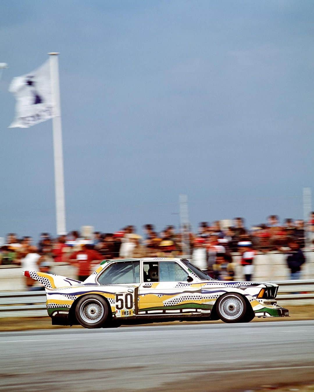 BMWのインスタグラム：「Happy 100th Birthday to the father of American Pop Art, Roy Lichtenstein! 🎂🎉   On what would have been his 100th birthday, we pay tribute to the genius behind the Ben-Day dots, comic-inspired art, and the 3rd edition of the #BMWArtCar. Lichtenstein was a trailblazing artist to the Pop Art movement in the 1950s and 1960s. Remembered for incorporating comic book imagery into traditional art, he challenged the fine art world with his style, clashing parody with documentary in his signature style. His technique involved meticulous hand-painted dots and lines, which he used when collaborating with BMW in 1977 for designing his Art Car.   Lichtenstein’s Art Car has remained one of the most popular ones to date. After he completed his version for the 1977 #320i, it premiered twice - as a work of art at the Centre Pompidou in Paris and as a racing car in the 24-hour race at Le Mans in June 1977. The car was driven by Hervé Poulain and Marcel Mignot from France, achieved ninth place in the overall rating, and finished first in its class.   “I wanted to use painted lines as a road, pointing the way for the car. The design also shows the scenery as it passes by. Even the sky and sunlight are to be seen … you could list all the things a car experiences – the only difference is that this car mirrors all these things even before it takes to the road.” - Roy Lichtenstein   @roylichtenstein   📸: 3rd Edition of the BMW Art Car by Roy Lichtenstein, 1977 BMW 320i Group 5 Race Version」