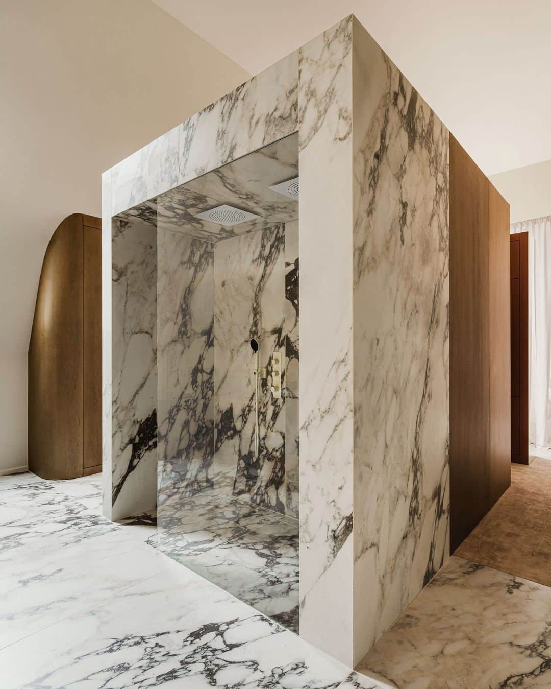 ELLE DECORのインスタグラム：「When conceiving the interior scheme of this 2,700-square-foot open-plan apartment, Polish designers Zuza and Piotr Paradowski (@paradowskistudio) made scale a priority. The opted to divide the spaces with hulking units they refer to as “blocks.” In the main bedroom, for instance, a freestanding monolith of Calacatta marble houses a decadent shower and abuts a Bordeaux-hued vanity on the opposite side. Was it a lot to digest when first described? The clients thought so. “They weren’t sure at first,” Zuza says of the couple. “But in the end they loved it.”  Click the link in the bio to tour the rest of this postmodern apartment, as featured in our November 2023 issue. Written by @charlescurkin. Photographed by @pionfotografia.」
