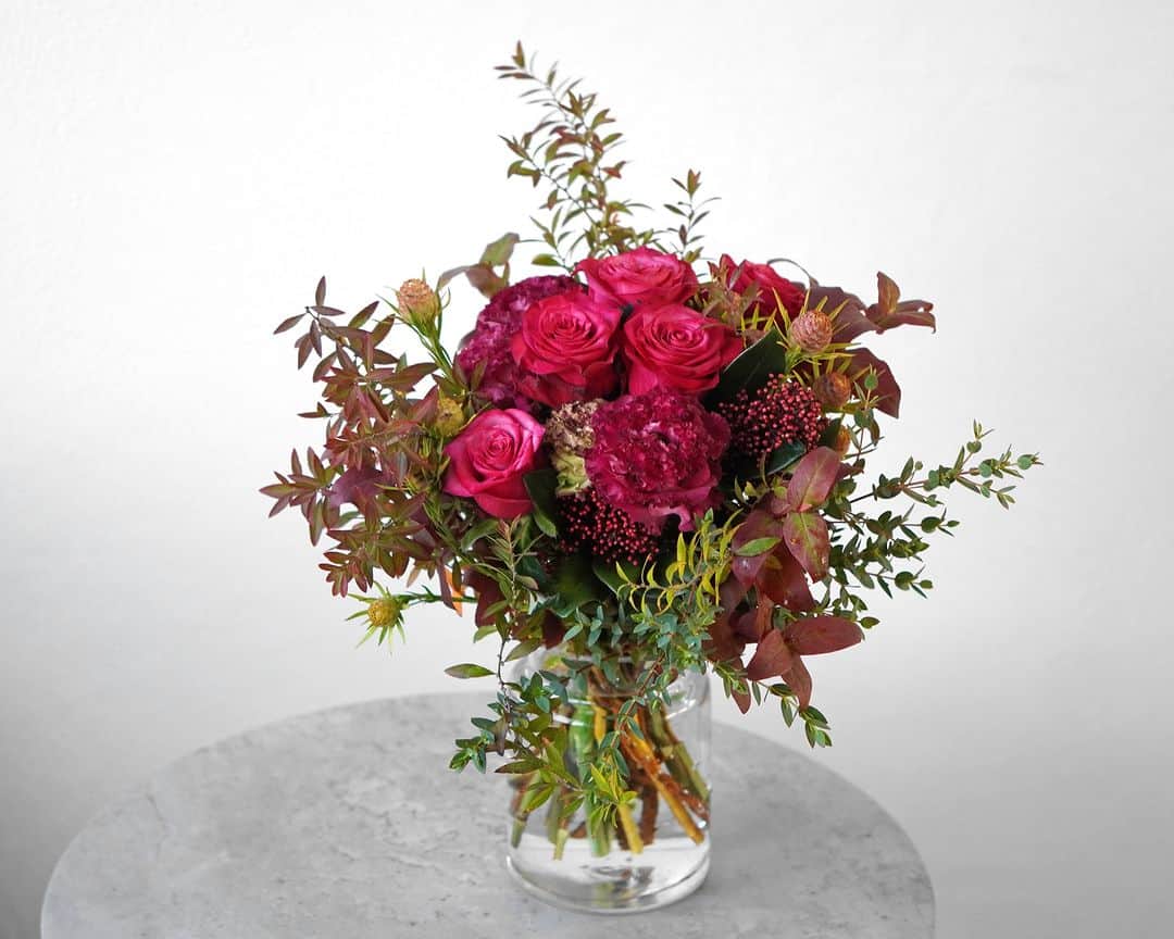 AOYAMA_HANAMOのインスタグラム：「深まる季節を感じる花合わせ。 ・ 濃いピンクの大輪バラやトルコキキョウに、赤く色づいたリーフや小ぶりなリューカデンドロン、赤いスキミアを添えて。全体的に落ち着いた花色でまとめ、シックな印象に仕上げた「#季節の花の定期便」です。 ・ プチプチとした可愛らしいつぼみをつけるスキミア。切り花としては、秋から冬にかけて流通しています。みかんに似た肉厚な葉が特徴で、赤だけではなく、爽やかなグリーンの品種もあります。フラワーギフトに使う際はつぼみの状態が多いですが、開花すると白い小さな花をたくさんつけます。アレンジメントやブーケにさりげなく趣を添える、名脇役です。 ・ 近頃は日も短くなり、ご自宅でゆっくりと過ごされる方も多いでしょうか。ぜひ、旬の花々と一緒に、秋の夜長をお楽しみください。 - - - #aoyamahanamo #青山花茂 #お花のある生活 #花が好きな人と繋がりたい #花を飾ろう #花のある暮らし #花のあるくらし #花のある日常 #癒しの花 #季節の花 #旬の花 #花のサブスク #フラワーサブスクリプション #お花の定期便 #季節の花の定期便 #季節の花の定期便プレミアムプラン #バラ #クシェル #スキミア #シキミア #トルコキキョウ #リューカデンドロン #花瓶活け #花束 #ブーケ」