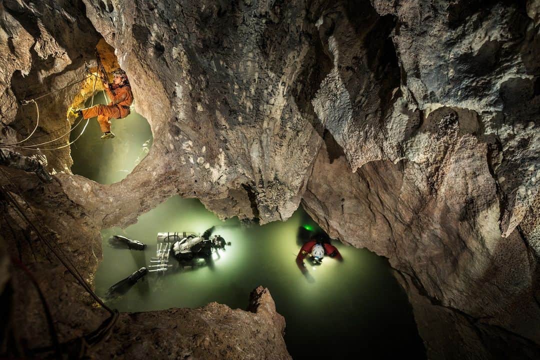 ナショナルジオグラフィックのインスタグラム：「Photos by @carstenpeter | From Earth’s surface to its subterranean caverns, some of the most alien habitats on Earth may come closest to comparing with Jupiter’s and Saturn’s icy moons and alien oceans.  In these images:  With support from caver Valentina Mariani, divers Kenny Broad and Nadir Quarta prepare to descend into Lago Verde in Italy’s Frasassi cave system. Initially, I was a bit underwhelmed by the little triangular entry, but after some rigging by Italian cavers, we managed to get high enough into the cavern. Only circuit diving assures that no oxygen “pollutes“ Lago Verde’s water, which is toxic to humans but rich in hydrogen sulfide and habitable for microbes with otherworldly metabolisms.  A caver hands sampling ampules to Broad. A little while later, he will discover a new gallery full of interesting microbial structures to collect.  A dirty and muddy environment is a challenge for geomicrobiologists Dani Buchheister and Jennifer Macalady to overcome as they process samples of biofilm collected in Lago Verde.  Flying a drone in Svalbard, Norway, numbed my fingertips for about two weeks. The blueish arctic twilight makes the area look like an icy moon. A small mountain formation, called a pingo, keeps a secret: a body of water rich in methane and hydrogen sulfide. Pingos are another strange habitat for specialized microbes.  Amid strong Arctic wind, astrobiologist Kevin Hand (kneeling, right) and microbiologist Dimitri Kalenitchenko (far right) drill into a pingo in Svalbard. The liquid they extract is almost instantly frozen. #WorldSpaceWeek  Read the full story at the link in bio.」
