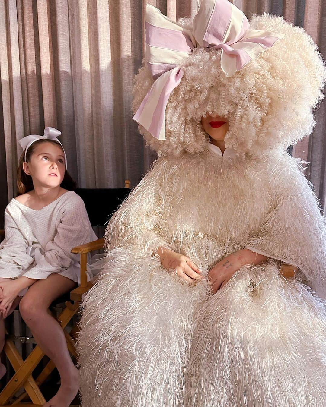 シーアのインスタグラム：「Waiting patiently ❣️ #GimmeLove - Team Sia  [image description: a girl with a bow sitting next to Sia in a big white dress and white wig]」