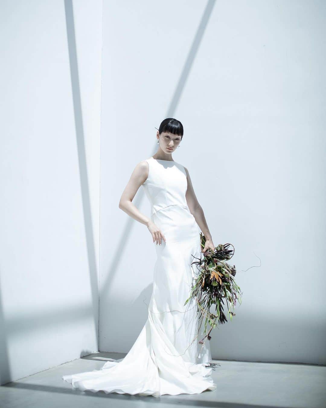 nae.ATELIERのインスタグラム：「nae.ATELIER 2023 new dress 【"isana"(イサーナ)】  派手ではないけれど、 モードでスタイリッシュなものがお好きな方へ向けてお作りしたマーメイドラインドレス。  鎖骨と肩の骨格を美しく印象的に見せるよう 直線的でスタイリッシュなネックラインとアームホールのラインに。  露出が少なくおさえ気味なフロントスタイルに対して、 大胆に開いたバックスタイルが 内に秘めた意志の強さを表現します。  体に心地よくフィットするストレッチ生地の上に、 柔らかく光を通す 美しいシルクオーガンジーを重ねたトレーンが 立ち姿のしなやかな曲線美を印象付ける ソフトマーメイドラインドレスです。  “Isana” is soft-mermaid line dress made of stretch fabric that comfortably fits the body, and beautiful silk organza for a train that allows soft light to pass through.  This dress is for brides that love modernity.  nae.ATELIER 東京都渋谷区恵比寿南1-13-2 EBISU COURT 101 TEL:03-6409-6369  #大好きと大切をすべてまとって #naeatelier #アトリエナエ #nae花嫁 #bridestyle #overseaswedding  #destinationwedding #elopementwedding #naebride #ウェディングドレス #シンプルドレス #isana」