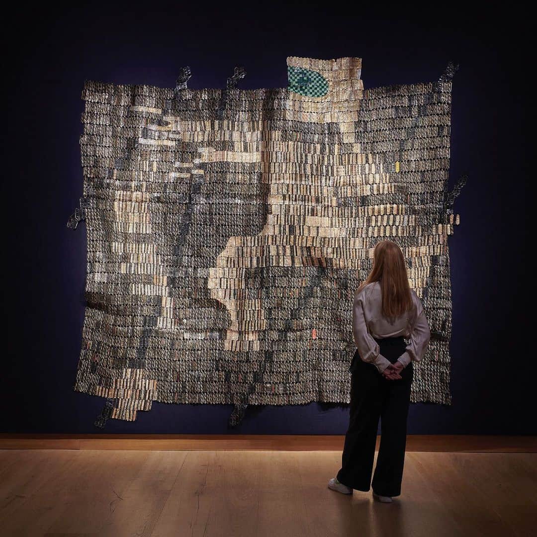 クリスティーズのインスタグラム：「'I let the material lead me. If it can't say something, then it better not be made to say it' - El Anatsui.⁣ ⁣ Spanning three-and-a-half metres across, 'Warrior' is a grand, shimmering example of El Anatsui's iconic bottle-top sculptures.⁣ ⁣ Made from thousands of flattened aluminium bottle-tops threaded together with copper wire, it represents a development in these works in its depiction of a legible human figure.⁣ ⁣ 'Warrior' will be offered in the 20th/21st Century: London Evening Sale this Friday, the same week the artist's  Turbine Hall commission at Tate Modern has been unveiled.⁣ ⁣ El Anatsui 'Warrior' (2015). Estimate: £700,000 – £1,000,000.⁣ ⁣ 📍20th/21st Century: London Evening Sale | Live Auction: 13 October, London.⁣ ⁣ #Frieze20 #ThisisLondon #londoncreates #elanatsui」