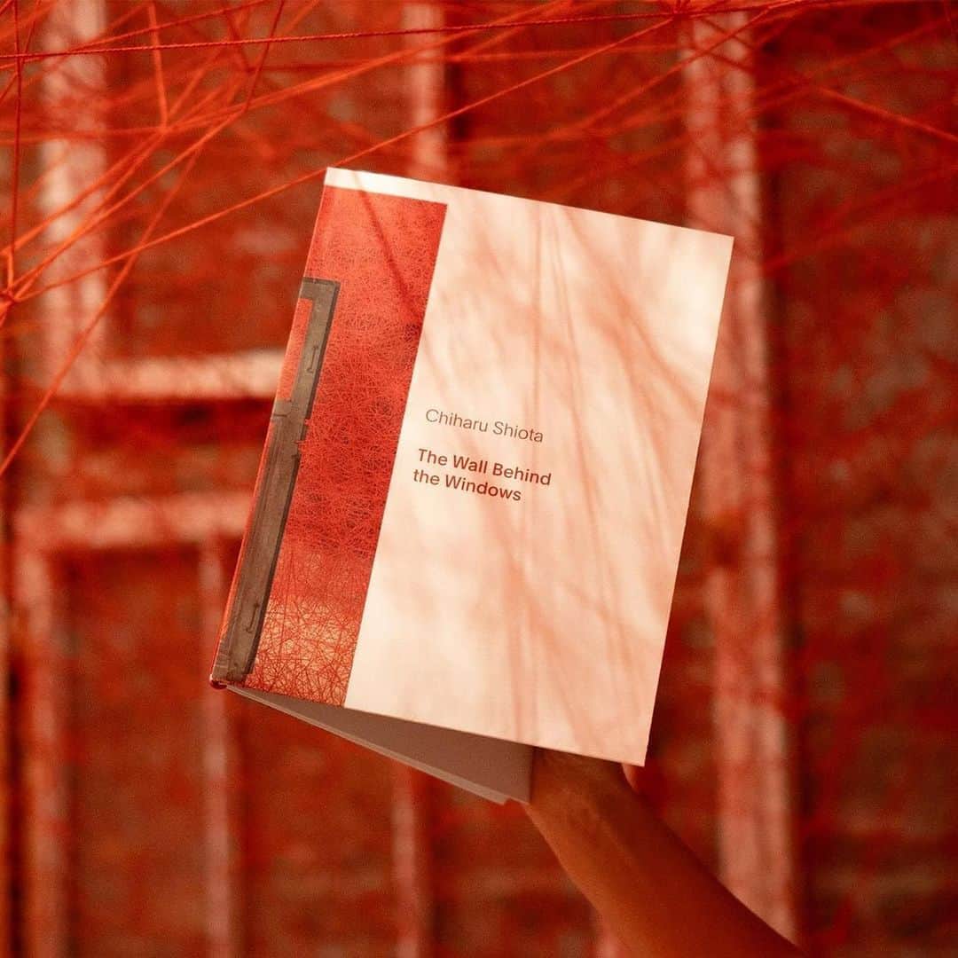 塩田千春のインスタグラム：「#Repost @koenig.souvenir ・・・ On the occasion of Chiharu Shiota's (@chiharushiota) solo exhibition THE WALL BEHIND THE WINDOWS in the Chapel of St. Agnes, KÖNIG GALERIE (@koeniggalerie) released an accompanying booklet sharing deeper insights into the artist's practice and the concept behind the exhibition. The leaflet includes two folded posters including three exclusive postcards.   For the installation, THE WALL BEHIND THE WINDOWS, Shiota endeavors to “reflect the unseen dimension of our ordinary life. It is like grasping something that is not there, but you can still feel it.” Within the space, Shiota hangs her windows within the room, but behind the windows, the wall remains. After two decades of working with windows as a material, Shiota is combining thread with windows for the very first time. While the artist fills the room with red thread, visualizing societal connections, she has placed a sewing machine at its center, conjuring the spectre of memory within the room, offering an occasion to empathize with the people that originally looked through these windows, from East to West. The artist points out that “The brick wall of the room is exposed behind the windows but engulfed in a web of connections. It is almost like a cocoon of memory.”  DETAILS Publisher: KÖNIG GALERIE Editor(s): Rosalie Pfleger in conversation with Chiharu Shiota, Colin Lang Binding: leaflet (two folded posters held together with rubber band including three exclusive postcards) Pages: 8 Dimensions: 210 x 275 mm Weight: 0.2 kg Language: English  Shop the booklet at our gallery store or online via link in bio!  #KönigSouvenir #KönigPublication #ChiharuShiota  Images by KÖNIG GALERIE © courtesy the artist and KÖNIG GALERIE」