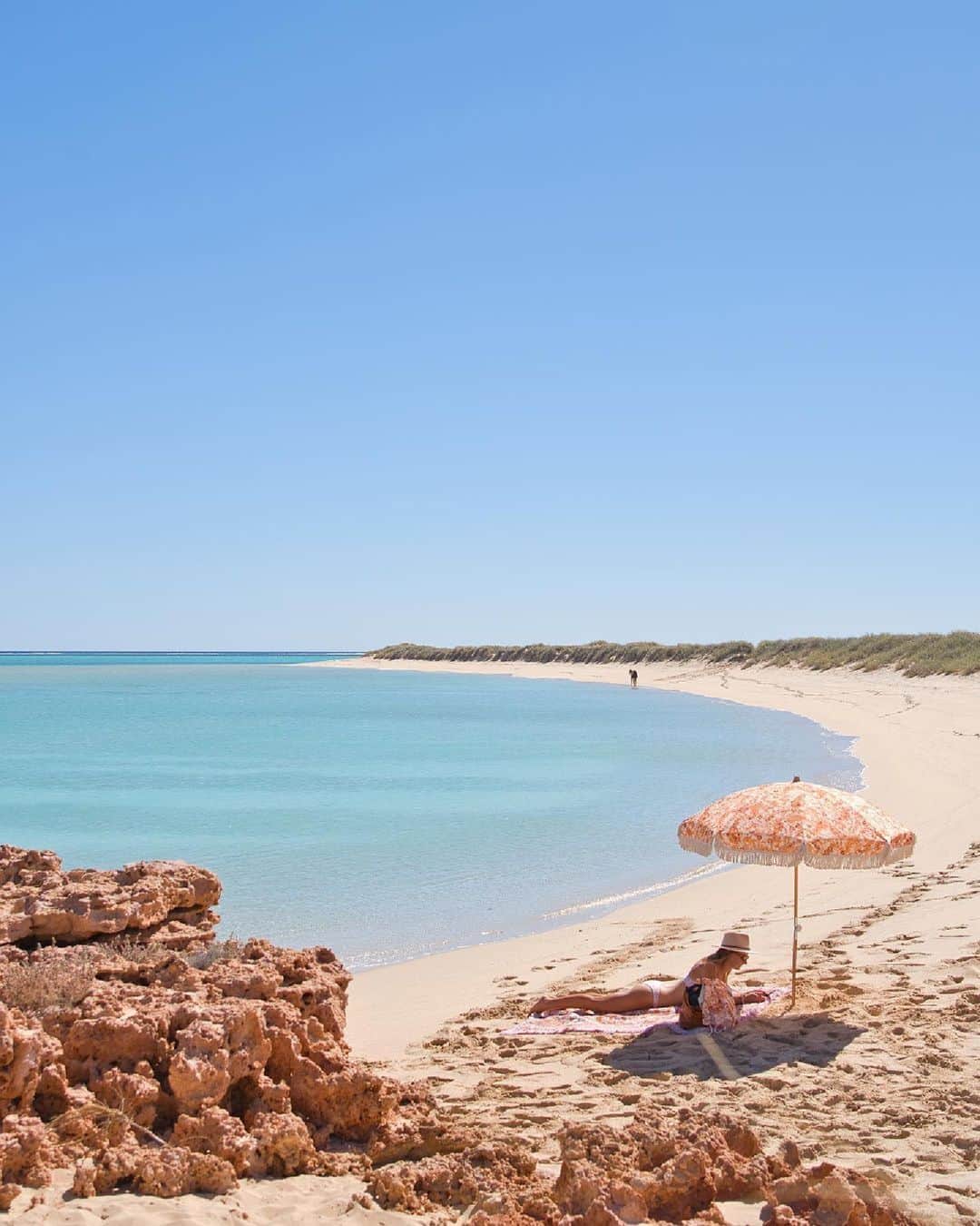 Australiaのインスタグラム：「It's official, @australiascoralcoast, we're on our way ✈️😎 This slice of pastel perfection captured by @our.australia.trip is truly a vision of bliss 🌸💛 Venture just beyond the stunning shores of @westernaustralia's #OspreyBay, and you'll reach @visitningaloo, where you can join @exmouthdiveandwhalesharks for an unforgettable swim with #WhaleSharks or #HumpbackWhales - sounds pretty incredible if you ask us! 🤷🐋  #SeeAustralia #ComeAndSayGday #WAtheDreamState #AustraliasCoralCoast #VisitNingaloo  ID: A young girl rests on a towel beneath a flower-patterned beach umbrella on pristine white sand. Soft blue water laps gently at the curved shore. Rocks frame the forefront of the image.」