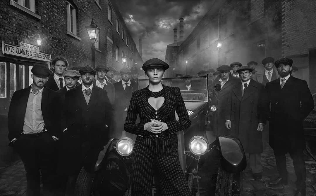 カーラ・デルヴィーニュのインスタグラム：「By Order of the Peaky Blinders  This photograph is an unapologetic nod to Steven Knight’s hugely popular 1920s British gangster series Peaky Blinders. With satanic chimneys belching smoke and cobbles awash with industrial grime, the period drama brought hellish industrial UK into our living rooms but did it with an admirable swagger and aesthetic genius. The anomaly of Peaky Blinders is that cinematography made hell look attractive.   Audiences around the world found themselves engaged by a new street subculture and sympathising with men with totally disposable moral fibre. Birmingham in the UK became known around the world for what it was portrayed to be like 100 years ago rather than what it is like now. That’s quite a trick.   My creative leaning was to twist the narrative a little. Cillian Murphy owned every scene in the series with a mesmerising intensity, but what if the leader of the gang was a woman? Most of the women in the series were depicted either as objects of lust or familial loyalty rather than necessarily agents of their own destiny. They faded into the scenery as often happens in mobster shows.   In my mindset there was only girl to go this job - the irrepressible force of nature that is Cara Delevingne. She owns this scene, just as Cillian did in the series, and that says it all. She is a national treasure and we are lucky to work with her as often as we do. As I often say to those that ask, “It’s her eyes”.   There was a big cast that day and everyone played their role. It only takes one person to kill the vibe and that evening everyone did a grand Peaky Blinders job. Maybe some of my extras have missed their vocation in life.  Thank you to our friends at @maddoxgallery for their help with putting this production on. We look forward to unveiling this image, alongside others from this shoot, at Maddox Gallery’s new space in Berkeley Street when our solo show starts on the 27th of October.」