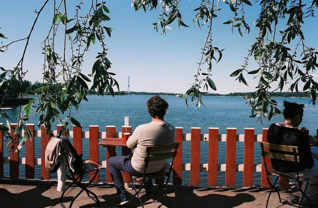 平岡佐智男さんのインスタグラム写真 - (平岡佐智男Instagram)「北欧新婚旅行13（北欧カフェ巡り3）：ソーセージは火のあるところで焼く  この日は20世紀を代表する建築家・デザイナーの一人であるアルヴァ・アアルトさんの家に行くことにしていた。 アアルト邸は一般公開していて人気のスポットだ。 ヘルシンキの左側、ヘルシンキ湾方面にある。  朝早く出発したので、アアルト邸がまだオープンしていないと言うこともあり、我々は行きたいと話し合っていた「cafe regatta」に行くことにした。  ヘルシンキ中央駅からバスに10分から15分ぐらい乗ったあと、10分ぐらい歩く。 わざわざいかないといけないカフェだが、ぜひわざわざ行ってほしい。 湖とコーヒーの素晴らしいヘルシンキを体感できる。 　  湖（海）に面したカフェで、イメージしていたフィンランドのカフェそのままだと思った。 名前の通り、大きなカヌーみたいなレガッタが湖に出され大人数でそれを漕いでいた。  丸太小屋のようなところにレジがあって、こちらで注文する。 もちろん英語など喋れないが、This one と、That's allがあればなんとかいける  　 シナモンロールとコーヒーを、妻は甘いドリンクを注文した。 シナモンロールを食べる時のパンクズを求めてカモメが木の上から狙っていたが、現地の人は慣れているのか、コーヒーの乗っていたお盆をたくみに振り回して、カモメを追い払っていた。  レガッタの名物に自分で焼くスタイルのウインナーがある。 レジでウインナーを買って、囲炉裏のようなところがあるので自分で焼いて食べるというものだ。 僕たちはこれをやってみたくて、ここに来た。  長い銛のような串にウインナーを刺して囲炉裏で焼いたのだが、火はそんなに燃えていなく、息を炭に吹きかけるとぱーっと赤くなるような状態で、こういう遠赤外線的な感じで焼くのかなと思っていた。  ウインナーを炭に近づけて5分、なかなか焼けないので炭の中にウインナー入れるパターンなんじゃない？などと妻と話し合って、ウインナーを炭の中に突っ込んでいたら、現地のボーイスカウトを毎週やってますみたいなお父さんが来て「、、、、手伝おうか？」と話しかけてくれた。 彼はおもむろに囲炉裏の隣の小屋から新しい薪を4本ぐらい持ってきて、その皮を剥いで投入し種火とすると、次に薪を入れると、あっという間にゴウゴウと火が起こり、ウインナーは一瞬で焼けた。  旅行者が火のないところで闇雲に炭の中にウインナーを突っ込んでいたのを見てられなくなったんだろう。優しい人だ。  一瞬で焼けた炭だらけのウインナーを齧りながら、お前らどこからきたんだ？と聞いてきたので、日本だ、と答えたが、すぐに日本だ、じゃねえよと思った。情けない限りだ！  その後、アメリカから来たおばあさんが横に座り、同じようにウインナーを焼きに来た。ゴウゴウと燃え盛る火でおばあちゃんのウインナーは一瞬で焼け「ニューエクスペリエンス」と僕に行ってきたので炭だらけのウインナーにマスタードをかけながら「ミートゥー」と答えた。  ーーーーーーーーーーーーーー  SACHIOPIA COFFEE 毎週月曜火曜8:00-21:00 東京都武蔵野市吉祥寺南町1-17-10　F＆Ｗビル１階2号室  ーーーーーーーーーーーー #旅行 #北欧 #海外 #海外旅行 #新婚旅行 #フィンランド #finland #caferegatta #旅行記 #旅行記録 #カフェ #カフェ巡り #北欧カフェ巡り」10月14日 9時00分 - sachio_coffeeforme