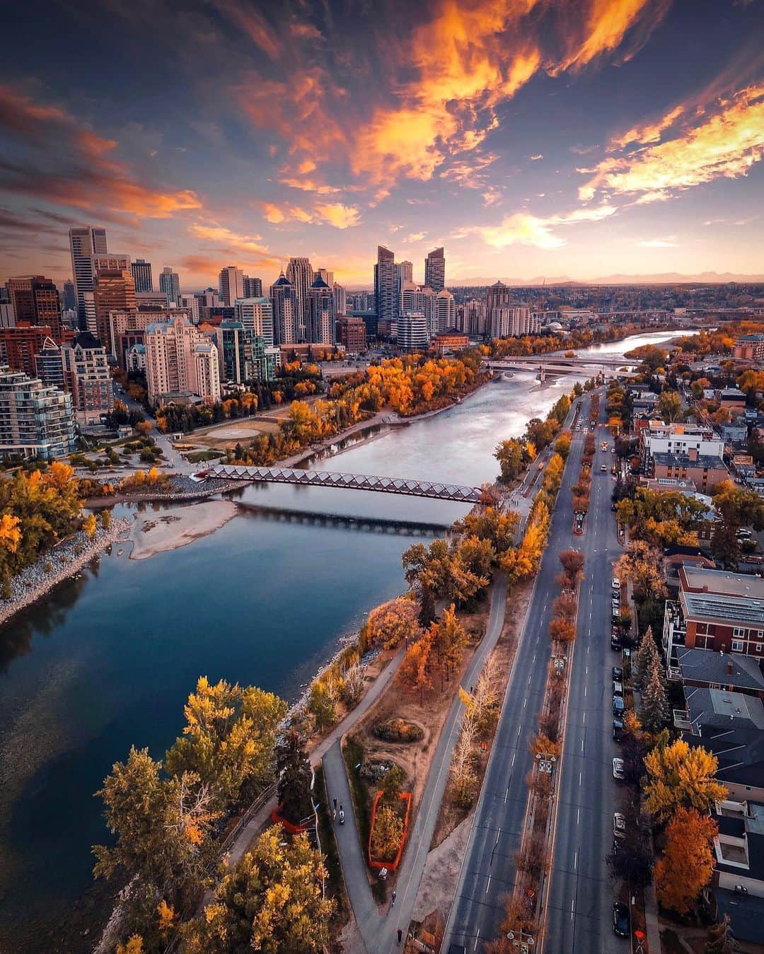 Explore Canadaのインスタグラム：「With vibrant colored trees, calm waters, and a stunning skyline, who could resist falling for Calgary’s autumn charm?   📷: @pushtheimpossible 📍: Calgary, Alberta, @tourismcalgary @travelalberta  #CaptureCalgary #ExploreAlberta #ExploreCanada  Image description: A bird’s eye view of Calgary’s skyline at sunset. A river sits in the middle of the city with an array of trees adorned in varying hues of orange, yellow, and green along its shore. Skyscrapers stand tall on the river’s bank.」