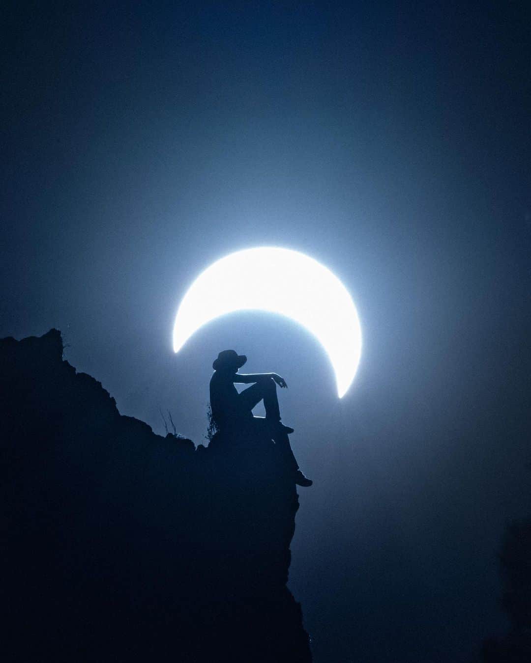 ナショナルジオグラフィックのインスタグラム：「Photo by @reuben | Today’s annular eclipse looms behind a hiker at the top of a pinnacle in Nevada's Schell Creek Range. An annular eclipse differs from a total eclipse in that the moon is slightly further away from Earth and doesn’t quite cover the sun's disk, creating a dramatic crescent and ring effect, rather than the total eclipse's visible corona amid full darkness. For more stories, follow me @reuben.」