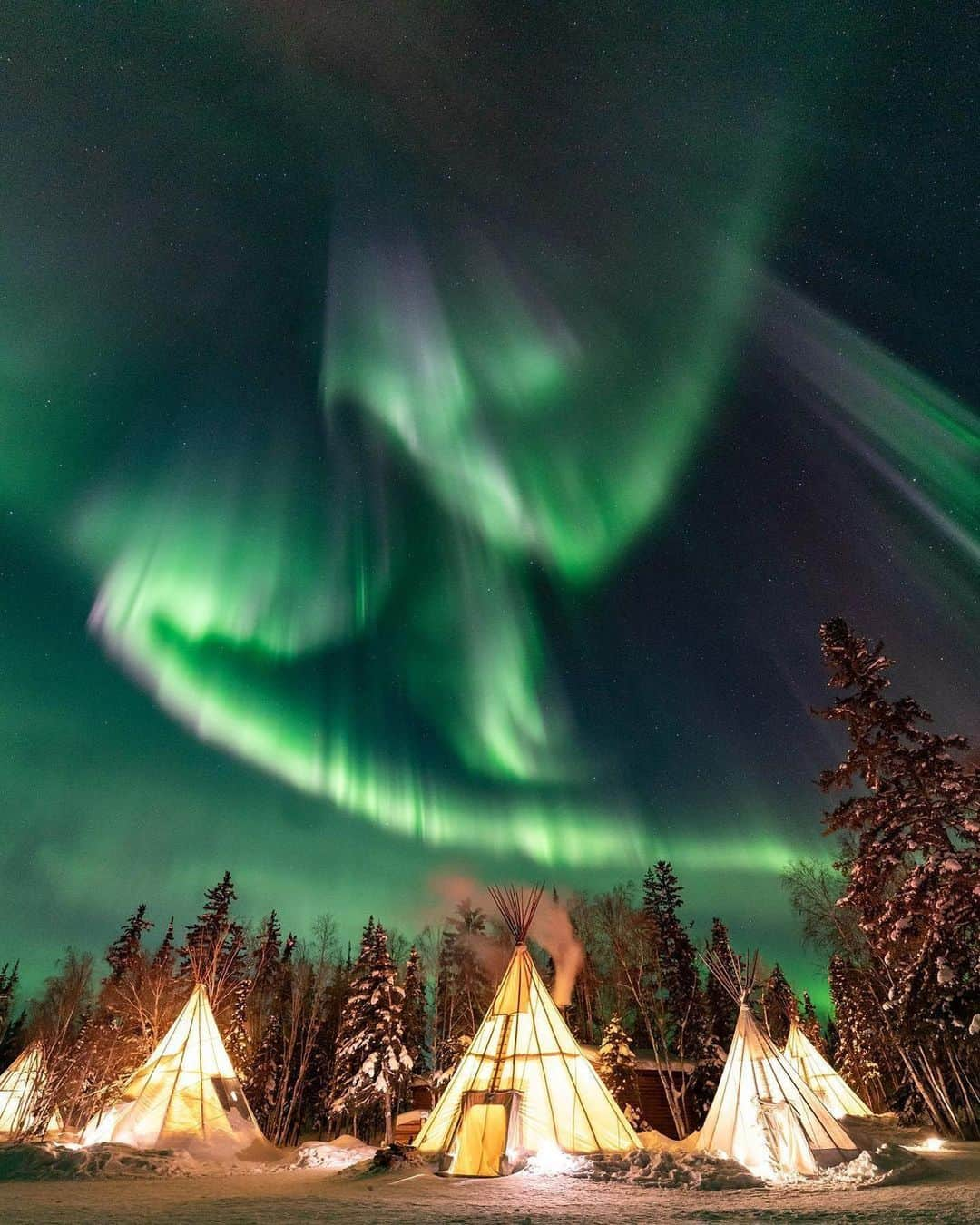 Explore Canadaさんのインスタグラム写真 - (Explore CanadaInstagram)「The Northwest Territories along with many parts of the country had an unprecedented summer. As many northerners evacuated their homes, the community rallied together to show support for one another highlighting the strength and spirit of NWT. As NWT welcomes the fall Aurora into the night skies, now is the time to support their local businesses. When will you visit?  📸1: @phill_picture 📸 2: @kailawalton 📸 3: @tashinaweagle  📍: Northwest Territories @spectacularnwt @auroravillageca #SpectacularNWT  Image description: Photo 1) Five glowing teepees are lined up with snowy trees behind them. Purple, white and green lights paint the dark night sky. Photo 2) Person looks out towards a vast snowy landscape. Snow covered trees can be seen in the distance. Flashes of green and purple light up a star-filled sky. Photo 3) Flashes of green light and gray clouds adorn a dark sky. The sky and a line of trees can be seen reflected off a body of water.」10月20日 1時30分 - explorecanada