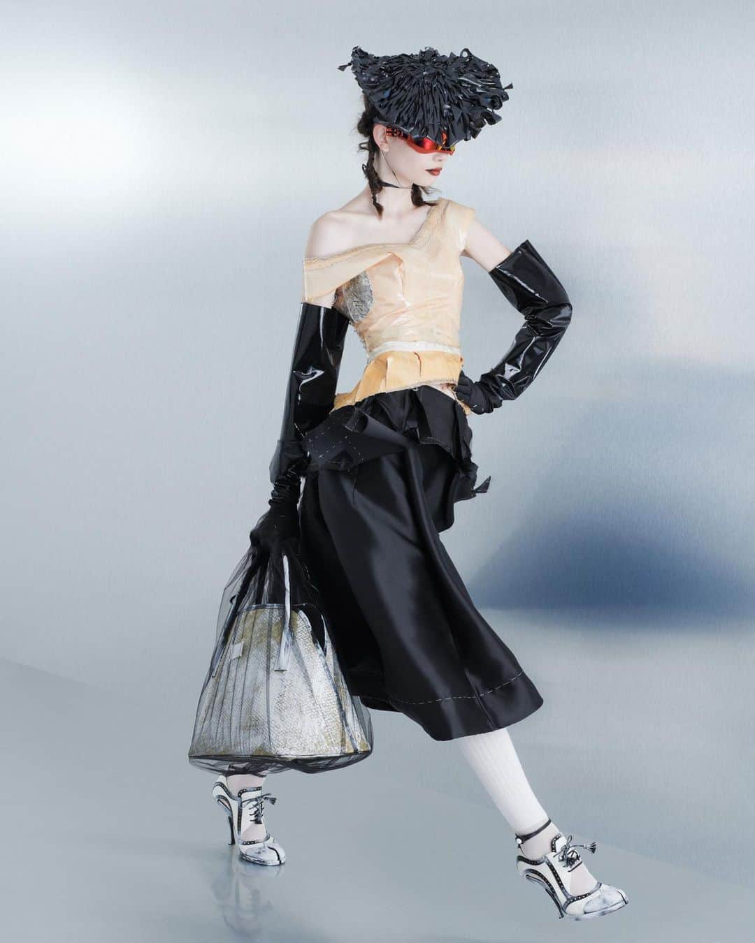 Maison Margielaのインスタグラム：「For the Spring-Summer 2024 Co-Ed Collection, Maison Margiela stages a search for individual truth reflected in the generational adaptation of an inherited wardrobe. Evoking the memory of one age through the radical eyes of the next, Creative Director John Galliano triggers a chemical reaction between eras and attitudes founded in a flashback narrative imagined within the Maison’s ongoing chronicle of the characters Count and Hen.  Look 29. Apricot viscose and taffeta decortiqué bustier applied with pressage worn with a black silk-mikado exfoliage skirt. Black binliner headpiece woven in the memory of a mid-century hat, Maison Margiela x Gentle Monster orange chrome robotic mask sunglasses, black dégradé rubberised opera gloves, white silk-cotton knee-high ribbon socks, bianchetto leather Tabi bourgeoise spectator pumps, and a bianchetto basket-weave shopper encased in a black tulle illusion carrier bag. Model Rezi Simonova  Look 31. Rose technical taffeta decortiqué bustier worn with a mushroom grey viscose exfoliage skirt applied with pressage. Black binliner headpiece woven in the memory of a mid-century hat, Maison Margiela x Gentle Monster white chrome robotic mask sunglasses, dove grey tulle illusion opera gloves, white silk-cotton knee-high ribbon socks, bianchetto leather Tabi monster sling-backs, and a bianchetto basket-weave shopper encased in a slate tulle illusion carrier bag. Model @elias_boussy」