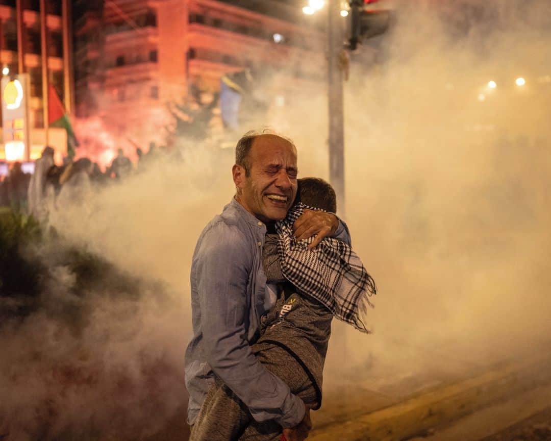 AFP通信のインスタグラム：「AFP Photo 📷 @angelos_tzortzinis - A man holds a boy as protesters run from tear gas launched by riot police during a rally in support of Palestinians, outside the outside the Israeli Embassy in Athens on October 18, 2023.」