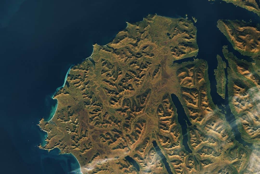 のインスタグラム：「Looks like Alaska has that #FallFeeling! 🍂  NASA / @USGSLandsat 9's Operational Land Imager 2 captured this view of the changing leaves on Kodiak Island, Alaska on October 3.   Image Description: A satellite image of the southwestern part of Alaska's Kodiak Island, showing a richly textured coastal area with many small hills and valleys glowing greenish-gold with fall foliage. The island covers most of the image from the right to the left, with deep blue water covering the left side of the image and extending inland via rivers and long, thin lakes. The land that borders the water is green inland, with a thin white beach visible across the island's curved upper edge.」