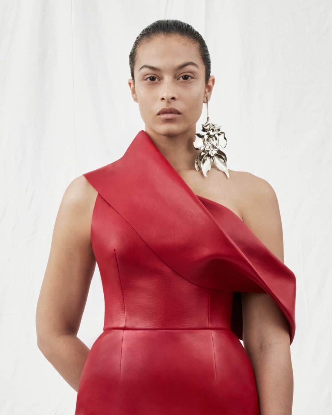 アレキサンダー・マックイーンのインスタグラム：「A pencil dress with an asymmetric drape neckline in red, worn with the Orchid Stick earring. ⁣ ⁣ Discover the #McQueenAW23 collection via the link in bio.⁣ ⁣ Photographed by @Jet.Swan」