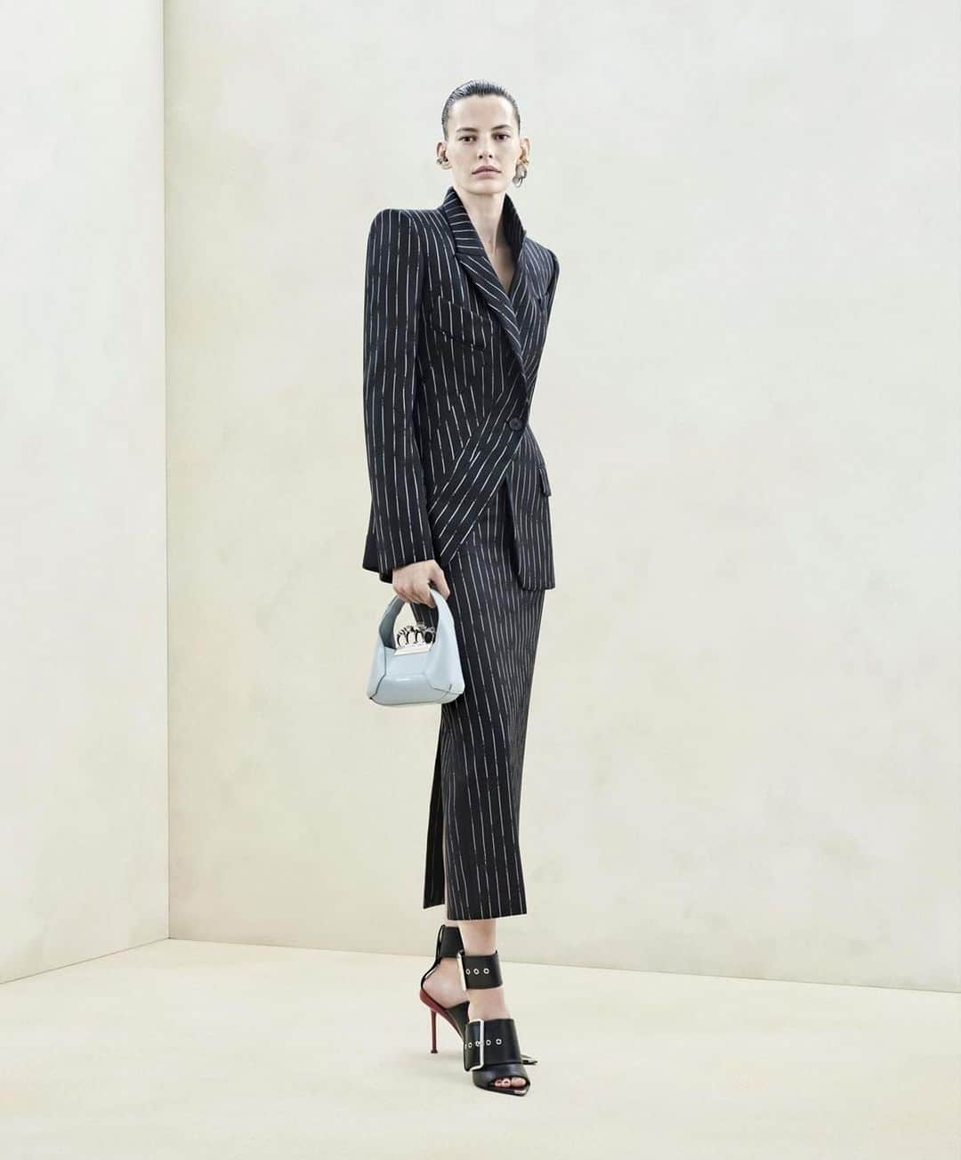 アマンダ・マーフィーのインスタグラム：「@alexandermcqueen #McqueenAW23 #SarahBurton ・・・ A black asymmetric tailored jacket and pencil skirt with a white broken pinstripe worn with the Mini #McQueenHoboBag and Punk Buckle sandals.⁣  Photographed by @Jet.Swan⁣ Video by @EbbaHult⁣ Track: Neurons by @roblewiscomposer⁣ Music Director: John Gosling @alexandermcqueen  Make up @lucia_pieroni Hair @simj45  Casting @jesshallettcast」