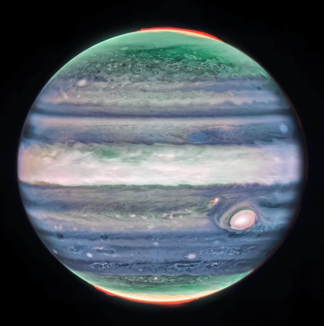 のインスタグラム：「🎶 Now that Webb's looking at the atmosphere/With winds of Jupiter in its stare...  @NASAWebb spotted a never-before-seen jet stream in Jupiter's atmosphere, offering more insight into how layers of the planet's atmosphere interact with each other.  Image description: Jupiter dominates the black background of space. The image is a composite, and shows Jupiter in enhanced color, featuring the planet’s turbulent Great Red Spot, which appears white here. The planet is striated with swirling horizontal stripes of neon turquoise, periwinkle, light pink, and cream. The stripes interact and mix at their edges like cream in coffee. Along both of the poles, the planet glows in turquoise. Bright orange auroras glow just above the planet’s surface at both poles.」