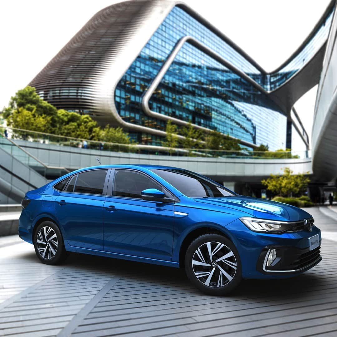 のインスタグラム：「O Novo Virtus é um sedan elegante, sofisticado e com muito conforto para motorista e passageiros. #VWBrasil #NovoVirtus  #VWParaTodos Imagem estática de um Novo Virtus azul visto de lado, estacionado na frente de um prédio com janelas de vidro.」