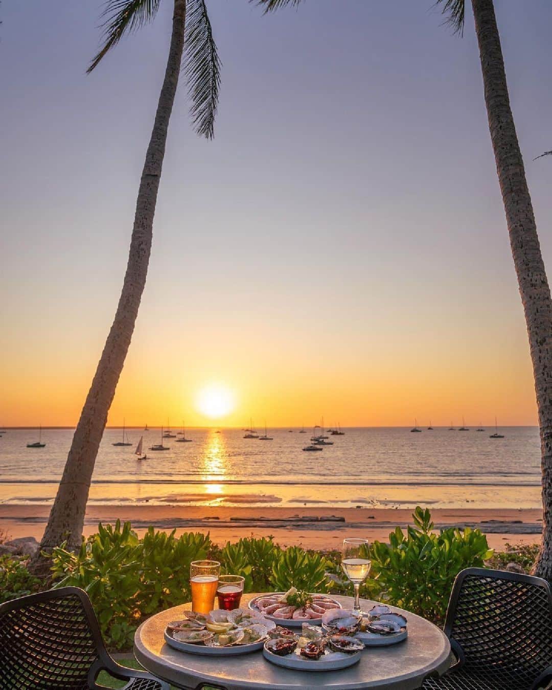 Australiaさんのインスタグラム写真 - (AustraliaInstagram)「Pull up a deckchair; we've saved you the best seat in the house! 🌞🍹 If balmy nights, colourful characters and outdoor adventures are on your #BucketList, you'll want to visit Gulumerrdgen (#Darwin) in @tourismtopend just like @_markfitz. After exploring the breathtaking national parks nearby (we're talking @litchfieldnationalpark, @seekakadu and #NitmilukNationalPark), sit back and relax at @thedarwinsailingclub for a drool-worthy seafood dinner while you watch the sun dip below the horizon.   #SeeAustralia #ComeAndSayGday #NTAustralia #TourismTopEnd  ID: a seafood spread and a few beverages are arranged on a small table set for two. Two palm trees frame the view from the table - a sandy beach at sunset. Sail boats are anchored just off the shore.」11月23日 18時00分 - australia