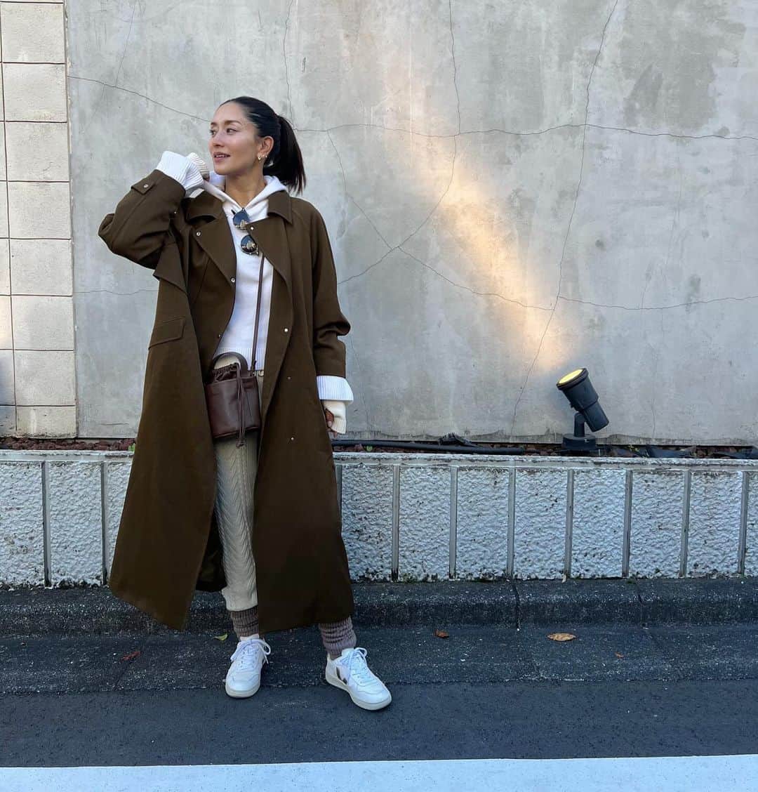 亀恭子のインスタグラム：「快晴で過ごしやすかった休日のお昼間。  @uncrave_official の オーバーシルエットのトレンチコートを。  適度な光沢と張り感がありつつ、しなやかな落ち感もある♡  この日はニットセットにスニーカー のカジュアルなスタイルにモダンなスパイスを。  スロートタブを留めてスタンドカラーにすると よりシャープな雰囲気なので 着こなしのバリエーションが楽しみ☺︎  someday's… #fashion #ootd #kkstyle #tokyo #kamescloset #coat #uncrave_white #knit & #pants #wrapinknot #armcover #etre #bag #thehighligts #shoes #veja #november #autumn」