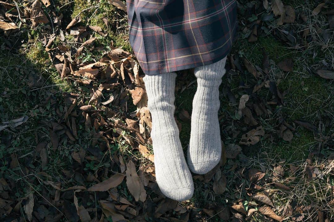 ヒラハルさんのインスタグラム写真 - (ヒラハルInstagram)「改良に改良を重ねる  “湯たんぽのようにあたたかい”が魅力のリブウール靴下。コンセプトでもあるこのキャッチフレーズは発売当初から変わらず伝え続けています。  わざわざのある長野県東御市は、真冬には氷点下となる日も多い地域です。この地域で寒さに負けずに快適に暮らしていくために、頼りとなったのが「ウール」でした。かねてよりウールの肌着や靴下を愛用していた代表・平田（ @rukaruka0315 ）。その優れた保温性・吸湿性を伝えながら、かつては他メーカーのウール靴下を店頭で扱っていました。ですが履き心地やデザイン性などあらゆる点において納得のいくウール靴下はなかなか見当たらず、探し続けていたのです。  ならば自ら作ろうと決めた2014年、ついにオリジナル靴下の企画が始まります。  このとき頼ったプロというのが、同じ長野県にあるタイコーさん（ @taikojapan.inc ）でした。大手アウトドア／スポーツブランドの靴下製造も手がけている大きなメーカーです。タイコーとの協働を経て、普通なら靴下に使わないという高級ウール糸を使った、湯たんぽのように温かい靴下が2014年冬に誕生したのでした。  また、「ホールガーメント製法」も発売当初から変わっていないポイントです。編み機から直接立体的に靴下を編成する製法で、縫い目がなく、手編みの靴下ようなやわらかい質感を出せるのが特徴です。特殊な技術を必要とするため、この製法ができる工場は全国でもそう多くありませんでした。  【補強に向けたアップデート①】 2014年登場のウール靴下はその冬に600足が完売。高級ウール糸にホールガーメント製法など、現在も変わらない点もある原型となりましたが、あたたかさにこだわるあまり耐久性に欠け、穴が空きやすいという課題がありました。  沢山のユーザーから頂いたご意見をもとに、再びタイコーと協議。穴の空きやすい部分の補強を求めて、翌2015年にアップデートを施します。靴下の裏側にナイロン糸を通すことで耐久性を高め、脱ぎ履きの際に爪が擦れて穴が空きやすいという課題をひとつ改善したのです。  このあとさらなる強度アップを目指し、糸を変えて試作を繰り返したこともありました。しかし肌触りの良さや経年変化の美しさが失われてしまうといった新たな課題も見られ、ウールの糸は変更しないことに。当初から変わらない仕様についても、何度も見直しを経てきたことで現在のリブウール靴下があります。  【補強に向けたアップデート②】 1度目のアップデートで「脱ぎ履きの際に穴が空きやすい」という課題は改善するも、そもそも摩耗への弱さは依然として残っています。使用している糸は通常の靴下に使わないような高級ウール糸。ものすごくやわらかく暖かく感じる反面、柔らかいので穴が空きやすいのです。  耐久性の高い糸を使えばより穴が空きにくい靴下になるでしょうが、「湯たんぽのように気持ちよく暖かい」というイメージは損なわれてしまいます。あくまで高級ウール糸の変更はせずに、2度目のアップデートを2019年に実施しました。  新たに、靴下の表側にウールとナイロンを一緒に編み込んで補強するという方法を採用しました。これにより、特につま先・かかと部分のウールの毛が靴との摩擦で抜けてしまい、生地が透けて薄くなったり穴が空いてしまうのを改善しました。  現在このウール靴下は、ウール83%／ポリエステル12%／ナイロン4％／ポリウレタン1％で作られています。発売後も試作と改良を何度も繰り返した結果、あたたかい、やわらかい、耐久性がある、フィット感を満遍なく表現できる、この配合に落ち着きました。  【それでも、穴は空いてしまうもの】 このように繰り返し改良を重ねてはいますが、高級ウール糸の性質上、どうしても穴が空きやすいのは事実です。ダーニング（刺繍のようにして穴を補修すること）をして大切に使い続けていただけたら幸いです。  ちなみに、洗濯は手洗いがベストではありますが、ネットに入れて洗濯機で洗っても大丈夫。愛着をもって使った分だけ長くご愛用いただける、そんな靴下に仕上がっているはずです。  ＊  わざわざでは「定番品しか作らない」をモットーに、オリジナル商品の企画開発に取り組んでいます。このウール靴下のように、改良を重ねられるのも、工場の生産工程を見直し続けられるのも、長く販売を続けている定番商品だからこそ。お客様には安定した品質で、適正な価格で商品を提供することができます。  ご紹介したリブウール靴下の誕生から現在に至るまでの改良の歴史を、より事細かに掲載しているのが「わざわざオリジナルの作りかた」の本です。ものづくりに興味のある方だけでなく、すでにウール靴下を愛用くださっている方や、これから愛用してくださる方にも、靴下とともにぜひ一度ご覧になっていただきたい1冊です。  ーーーわざわざの読み物「改良に改良を重ねる」より  🤞お買い物はプロフィールリンクより 『わざわざオンラインストア https://waza2.com/』をタップ  ・・・・・・・・・・・・・・・ #パンと日用品の店わざわざ #わざわざ #wazawaza #わざわざオリジナル #わざわざの靴下 #ウール靴下 #リブウール靴下」10月31日 17時41分 - wazawazapan
