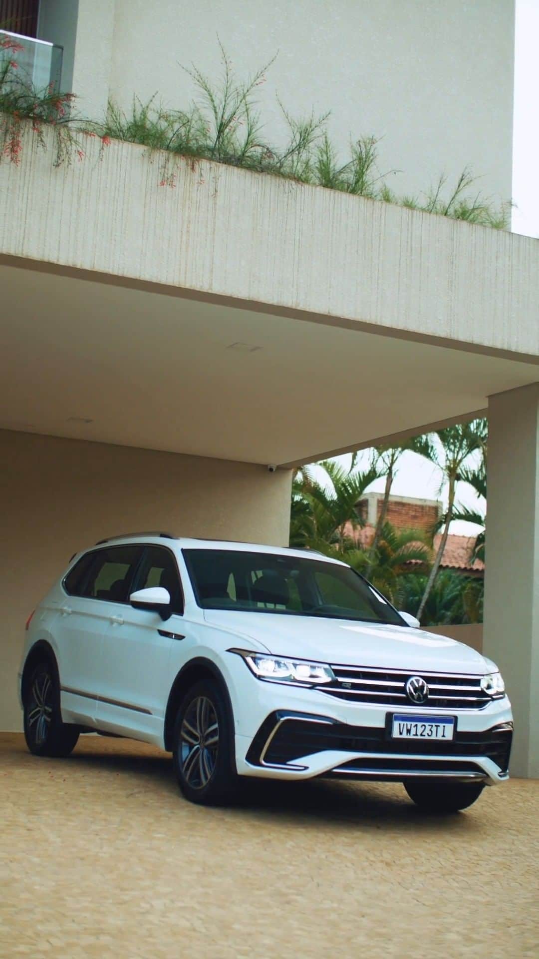 のインスタグラム：「Tiguan Allspace R-line está voltando e, agora, com mais elegância, tecnologia e segurança. E, claro, mais espaço: são 7 lugares para você compartilhar com a família e os amigos com muito conforto. Estamos preparando uma surpresa incrível e você é nosso convidado especial, entre em contato com o concessionário mais próximo e garanta seu convite para participar. #VWBrasil #NovoTiguan   #vwpratodos: Começa com uma cena do Tiguan Allspace R-Line, branco, parado na garagem, mostrando closes do seu design exterior. Em seguida, vemos cenas do espaço interno, tecnologias e funcionalidades.  Foto de um Tiguan Allspace R-Line, branco, estacionado na rua, em uma cidade, em frente a um prédio. Na segunda foto, vemos um close da frente do SUVW. Na última foto, vemos um close da parte traseira do carro, com foco no porta-malas.」