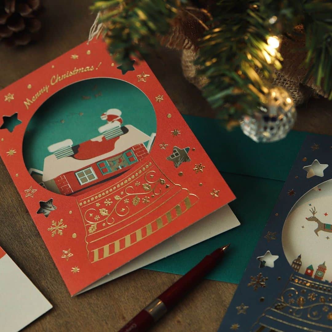 RYU-RYUのインスタグラム：「🎄新商品のお知らせ🎄 . 【クリスマスグリーティングカード】 . こんばんは！ 本日も新商品のクリスマスカードをご紹介します🎅 . スノードームをイメージした クリスマスのグリーティングカードです🎄 . 金箔を贅沢に使用した表紙の型抜き部分からは 内側に印刷されたイラストが覗きます✨ イラストの積もった雪の部分に メッセージを書くこともできます📝 . カードに合わせた色使いの封筒付きで 定型郵便での郵送も可能です📮 . 外国の絵本のようなカードは 受け取った後も 飾っておきたくなる可愛さですよ✨ . 【クリスマスグリーティングカード】 カード1枚/封筒1枚(定形) 本体価格380円＋税 . こちらの商品は リュリュのオンラインショップ 『リュリュマーケット』でも ご購入頂けます😊 プロフィール画面から アクセスしてくださいね🎅 . #ryuryu #リュリュ #雑貨 #ステーショナリー #文具 #クリスマス #クリスマスカード #クリスマスツリー #オーナメント #プレゼント #ミニカード #タグカード #ラッピング #ホログラム #サンタクロース #ギフト #ジングルベル #メリークリスマス #グリーティングカード #グリーティング #スノードーム」