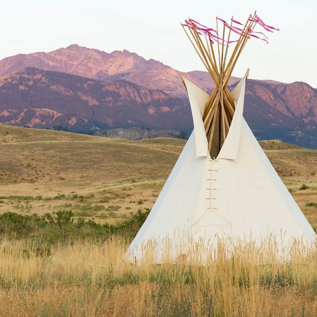 アメリカ内務省のインスタグラム：「Happy Native American Heritage Month! Interior is proud to celebrate the traditions, languages and stories of Native American, Alaska Native, Native Hawaiian and Island communities and ensure their rich histories and contributions continue to thrive with each passing generation.    Photo by Jacob W. Frank / NPS   #NativeAmericanHeritageMonth   Alt Text: A teepee in a valley during sunrise with tall mountains in the distance.」