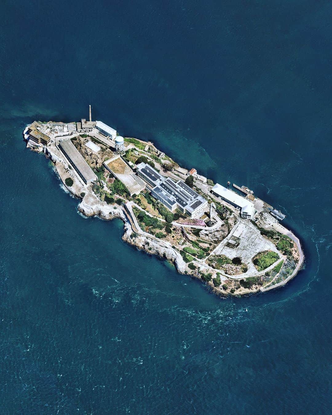 Daily Overviewのインスタグラム：「Alcatraz is a small island 1.25 miles (2 km) offshore from San Francisco, California. Originally developed in the mid-19th century with a lighthouse and military fortifications, Alcatraz was converted into a federal prison in 1934. Strong currents around the island and cold water temperatures made escape nearly impossible, earning Alcatraz Federal Penitentiary a reputation as one of the most notorious prisons in American history. The prison closed in 1963, and the island is now a major tourist attraction.  Created by @dailyoverview Source imagery: @nearmap」