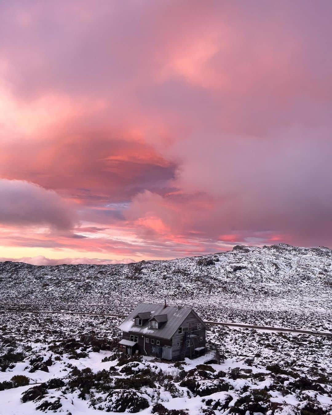 Australiaのインスタグラム：「We love a pop of pink! 💕 Captured by @time_we_travel, this vibrant landscape beneath a brilliant sky is the kind of pure magic you'll find throughout #BenLomondNationalPark in @visitnortherntasmania ✨ Sleep in luxury at @peppersilohotel in #Launceston, lutruwita (@tasmania) before making the one hour journey to this @tasmaniaparks for jaw-dropping hikes. Plan your trip in #winter for snow-capped views like this 👆❄️   #SeeAustralia #ComeAndSayGday #DiscoverTasmania #VisitNorthernTasmania  ID: A house sitting in a snow covered field under a cloudy sky filled with pink hues of sunset.」