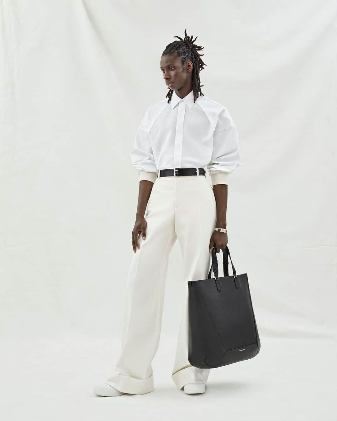 アレキサンダー・マックイーンのインスタグラム：「A shirt with dropped harness shoulders in white cotton poplin and wide-legged trousers with turn-ups in white cotton gabardine. Paired with a black belt and the Edge tote bag.⁣ ⁣ Discover the new #McQueenMenPreSS24 collection via the link in bio.⁣⁣ ⁣⁣ Photographed by @Jet.Swan ⁣⁣ Video by @EbbaHult ⁣⁣ Track: Indigo by Hit By A Rock⁣⁣ Music Director: John Gosling」