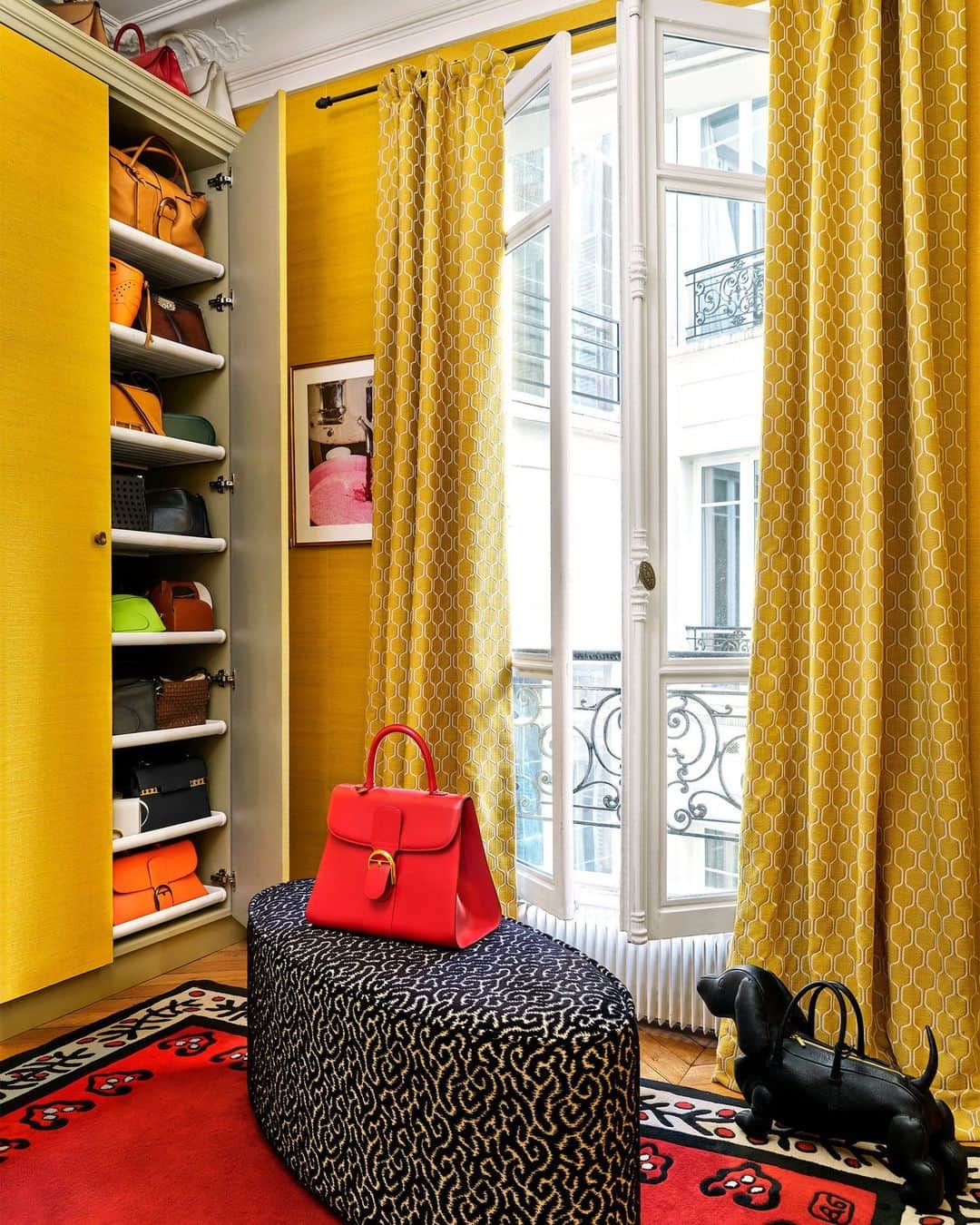 ELLE DECORのインスタグラム：「What does the closet of an accessories designer look like? Observe: In this mustard-yellow boudoir, an array of handbags designed by homeowner Marc Valeanu (@marcvaleanu) for @delvaux, @berluti, and @lanvin fills the closet. The ottoman is in a @lamaisonpierrefrey fabric, and the rug is by Garouste & Bonetti. The red handbag is by Delvaux and the dog-shaped handbag is by @thombrowne.   Click the link in the bio to tour the rest of this colorful Parisian apartment, as featured in our November 2023 issue. Written by @gaygassmann. Styled by @oliviagregorystylist.」