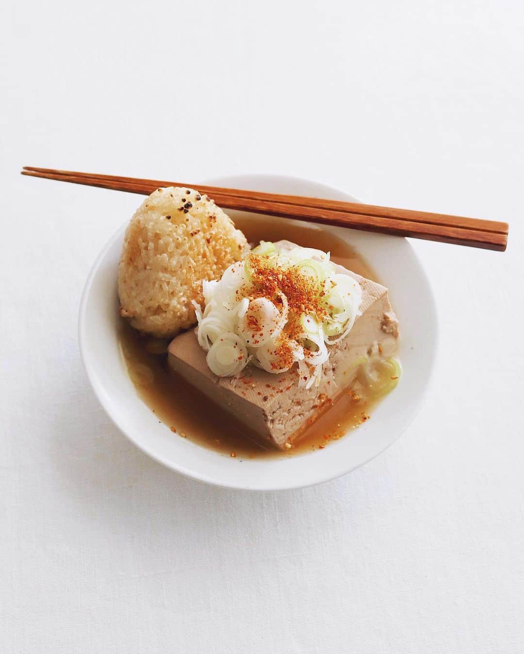 樋口正樹のインスタグラム：「Tofu oden & Yakionigiri 🍙  晩酌の〆におでんの豆腐に 焼きおにぎりを浸した一品。 とうめしのイメージなので 刻みネギと七味はたっぷり😋  . #とうめし #豆腐おでん #焼きおにぎり #〆 #シメ #tomeshi #tofumeshi #yakionigiri #onigiriaction」