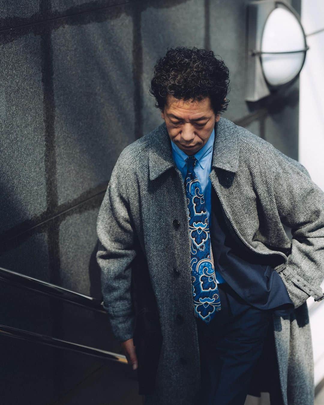 のインスタグラム：「今、着たい。私の本命アウター。〜’23 Autumn Winter〜  ビームス ハウス メン 横浜 田中和也  「ここ数年、ゆったりとしたシルエットのコートが気分ですね。こちらの〈ビームスF〉のベルテッドコートは、一枚袖ならではの優雅に流れる肩の落ち感と、裾にかけて柔らかく広がるAラインのシルエットがクラシックな趣き。目の詰まった重みあるヘリンボーン生地を載せ、さらにその重厚な空気感を増して表現された一着です。ウエストのベルトをギュッと絞り、シルエットに変化をつけてスッキリとこなす着方も好きですが、このぐらいヘリテージな顔つきであればやはり男らしく、ガバッと羽織りたくなります。カジュアルなスタイルも得意とするこのコート、スーツにはまず間違いありません。ネイビーソリッドのスーツにタブカラーシャツとペイズリータイのストイックな装いも、軽くないほどよい重さの塩梅で見せてくれます。機能面で言えば、ダウンなどのハイスペックなアイテムが便利な昨今ですが、私は専らヘリテージ派。素朴な風合いにこそ惹かれます」  #mrbeams #beams #beamsf #brillaperilgusto #mensfashion」