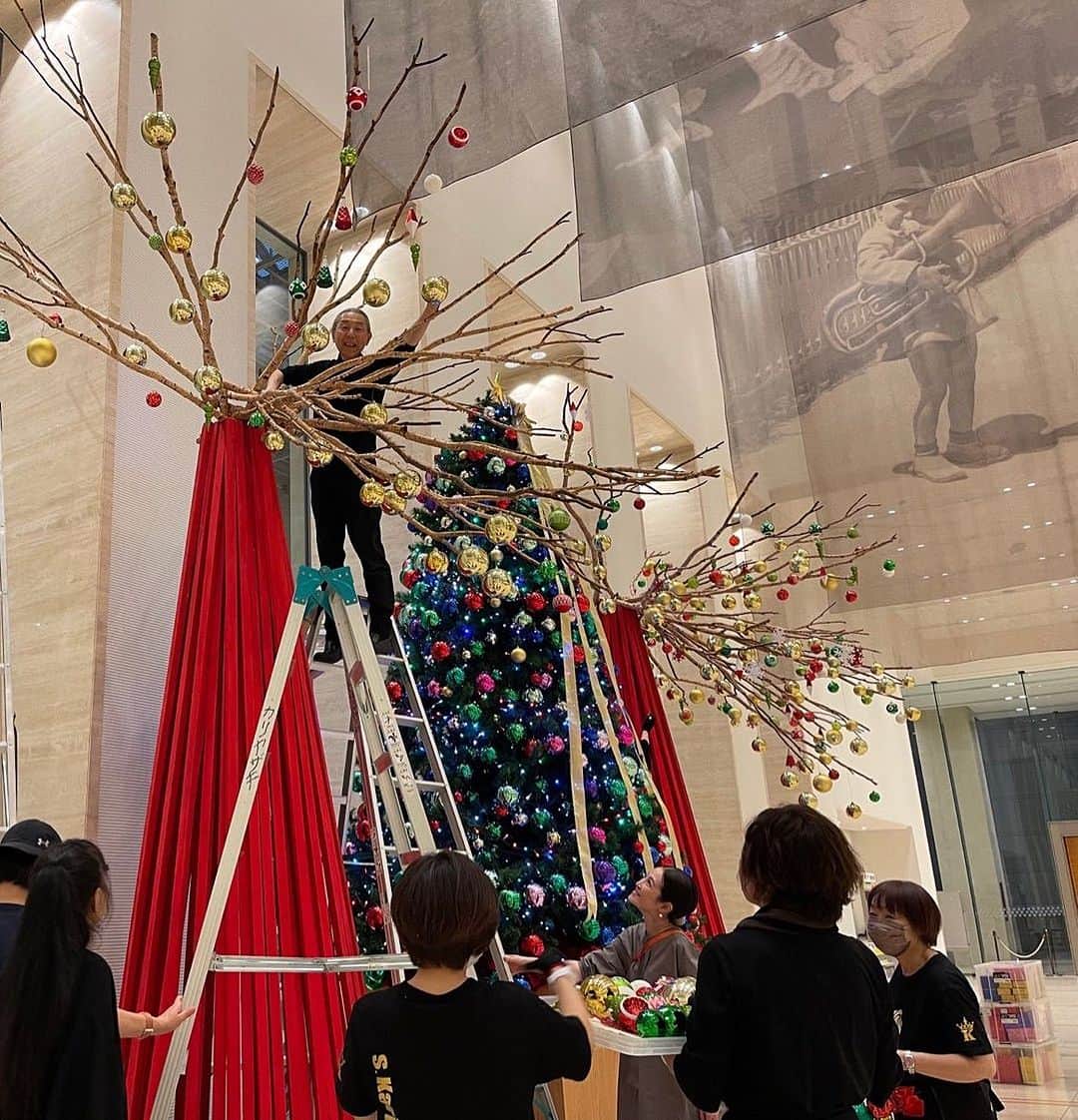 假屋崎省吾のインスタグラム：「東京オペラシティコンサートホールロビーに恒例のクリスマスツリーを花教室の生徒さんもお手伝いいただき、巨大な作品を制作してきました〜っ✨  高さ４メートルはあり、命懸けの搬入😎  目を見張るばかりの傑作が出来上がりましたよ〜っ🙌  #假屋崎省吾 #カーリー #東京オペラシティ #コンサートホール #クリスマス #ツリー #装飾 #イベント」