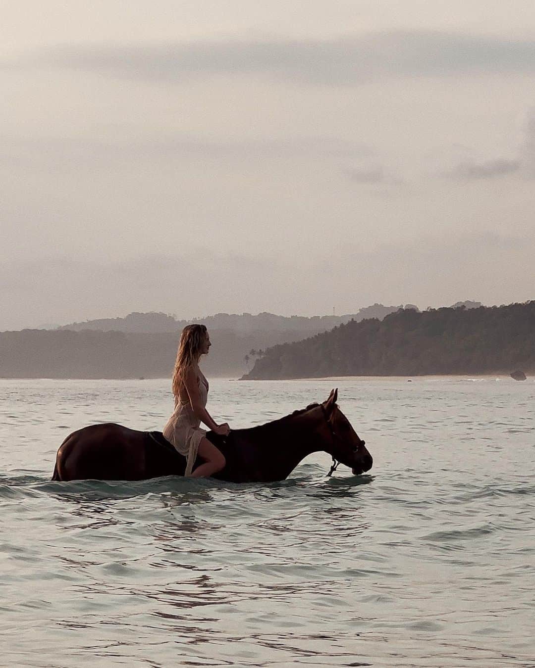 ニオミ・スマートのインスタグラム：「Connecting with Elton 🐴. I was told before meeting Elton that he can be an unsociable and introverted horse, and nervous at times. I have little experience with horses, but I decided to take some time before the walk on the beach to get to know this magnificent being. I was feeling a little nervous too.   I spoke softly in his ear that I understood, that I’m also a bit of an introvert, and it’s ok if he wants to stay in the stables but if he chooses to join me we can stop at any point. Thankfully he forgave me for mistaking his name for Elvis…   Elton chose to join me for a walk along the beach and even a swim in the sea - I was surprised how eager he was to immerse himself into the water 🌊.  We stayed in the water for a peaceful few moments, with him nuzzling his nose into me whenever I paused from stoking his nose and ears. We shared a few secrets and stories too ✨.   Honestly, this was one of the most heartwarming encounters with an animal I have experienced. I may be completely wrong and sugarcoating the whole thing, but it felt like taking that moment to connect and bond before taking part in this experience made a world of a difference to both Elton and myself to put us both at ease.   I don’t know whether animals can understand our words specifically, but they most certainly feel the energy of our presence and vibration of our voice.   Animals are truly a gift. The bond we can form with them feels so pure, like unconditional love. 🤍  Thank you to @nihi for this memorable experience.」