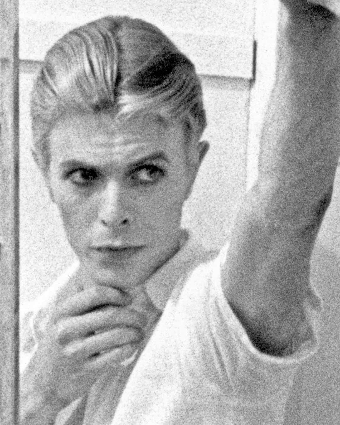 デヴィッド・ボウイのインスタグラム：「Please forgive the graininess of our latest Bowie Reflection. It’s an enlargement of TJ Newton (Bowie) on the set of The Man Who Fell To Earth, taken by David James.   Here’s the caption from the reverse of the uncropped photo: “Mary-Lou (CANDY CLARK) tries to break down formal barriers between herself and Thomas Jerome Newton (DAVID BOWIE) when she invites him into her bathroom.”  The second image is of Bowie’s original artwork (see signature bottom right), a collage he created utilising two other stills from the same scene.  If you’re unfamiliar with this piece, it first appeared as a full-page in the 1976 ISOLAR tour programme and it was also an exhibit at the David Bowie Is V&A exhibition. (See last image)  Look closely at Bowie’s reflection and the bubbles in the bath. A bit of pre-Photoshop scalpel work by Bowie.  Thankfully, his replacement of the bubbles with Linoleum keeps us on the right side of social platform censors. The original image of Mary Lou was a little more revealing.   #BowieReflections」