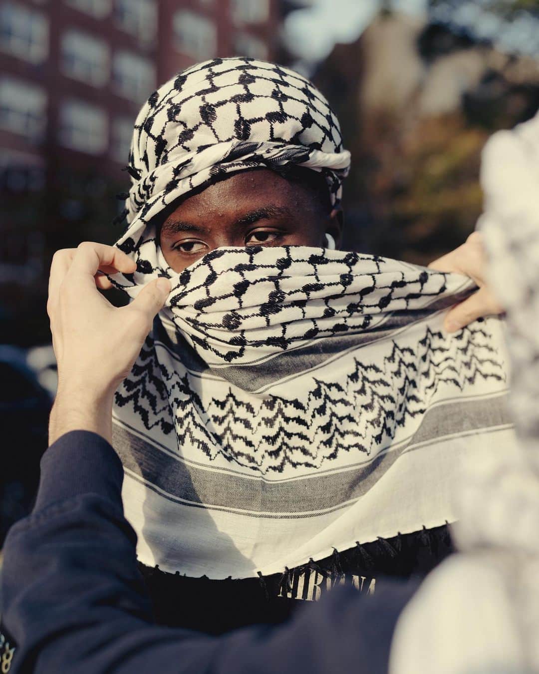 New York Times Fashionのインスタグラム：「As demonstrations have cropped up globally in support of civilians in Gaza, some Palestinians have been encouraging non-Palestinians to wear kaffiyehs, the square checkered scarves traditionally worn in parts of the Middle East, as a show of solidarity.  The black-and-white version in particular has become a badge of Palestinian identity, with many Palestinians wearing it at events like weddings and graduations. The kaffiyeh has also been adopted by Palestinians as a symbol of their aspiration and long struggle for independence, making it divisive to those who associate it with the fighting involved in that struggle.  Tap the link in our bio to learn more about the significance of this garment. Photos by @amirbangs」