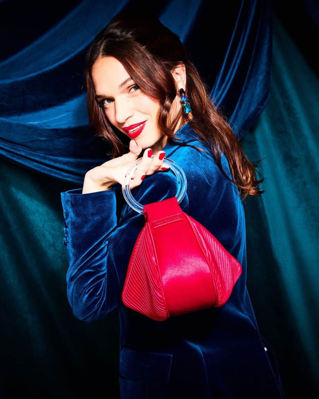 ルルギネスのインスタグラム：「Elevate your party style with Cleo, a retro-inspired evening bag that's pure glamour. In Lulu Red satin, it sports a signature 'croissant' shape and chic acrylic bangle handles. It's all about the fabulous details, from the concealed magnetic fastening to the shiny gold lip zip puller with the L.G. monogram.   Tap to shop.  #LuluGuinness」
