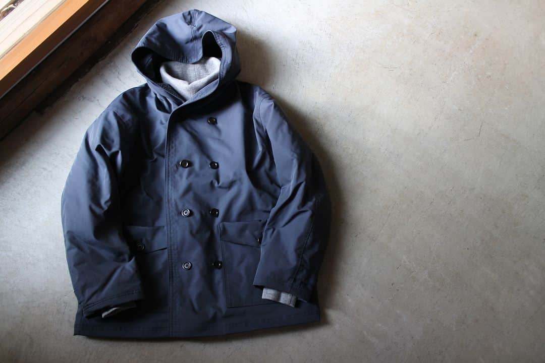 Jackmanのインスタグラム：「▽ FW23 OX SPECTATOR SHORT COAT JM8383 100%POLYESTER ￥44,000 Color:107 Dark Blue Gray  ポリエステルフィラメント糸で 織り上げたオックスフォード織りの 布帛素材を使用した フーディコートです  ポリエステル糸の中では 太めの番手の糸を200本も束ねて しなやかで鈍い光沢と 高い強度を実現しました  デザインは着回しの幅が広い ショート丈ですが 中綿入りで大ぶりのポケットと フードが付き 観戦には最適なアウターに 仕上げました  またインナーの着用を考えて 肩巾と身巾はゆったりした 設計にしました  ファン感謝デー用に ぜひ  インナーは JM7366 GG Sweat Highneck 今シーズン久しぶりに復活した しっかり暖かいハイネック仕様です  This Hoody coat utilizes Oxford fabric woven with polyester filament yarn. By bundling as many as 200 strands of thicker-than-average polyester threads, we’ve achieved a flexible material with a subtle sheen and high strength. Its short length lends it to mixing and matching, but it also features insulation, large pockets, and a hood, making it perfect outerwear for spectating. We’ve designed it with a generous shoulder and body width to accommodate inner wear.」