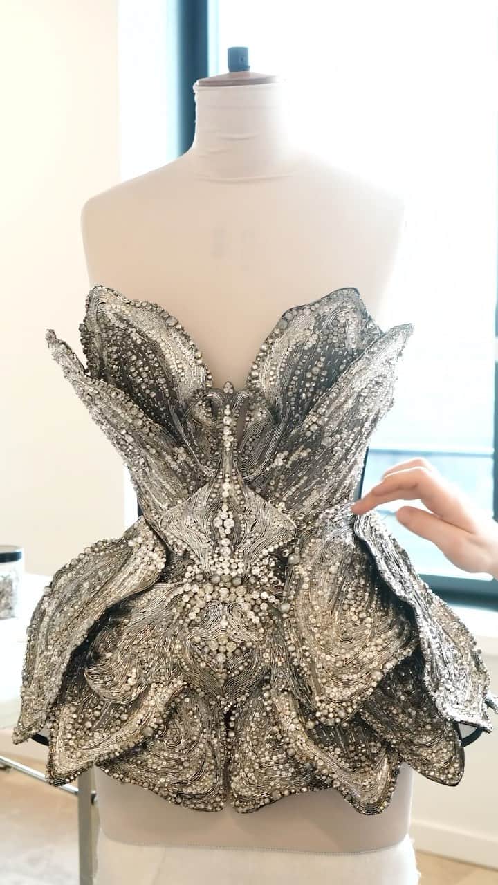 アレキサンダー・マックイーンのインスタグラム：「3D orchid petals made from silver threadwork and beads are delicately hand-placed onto a corset bodice with an invisible tulle base. Adorned with hand-embroidered crystal beads, the look is finished with matching Pin heel boots.  Discover #McQueenAW23 via the link in bio.  Music Director: John Gosling Track: Landing by Rob Lewis」