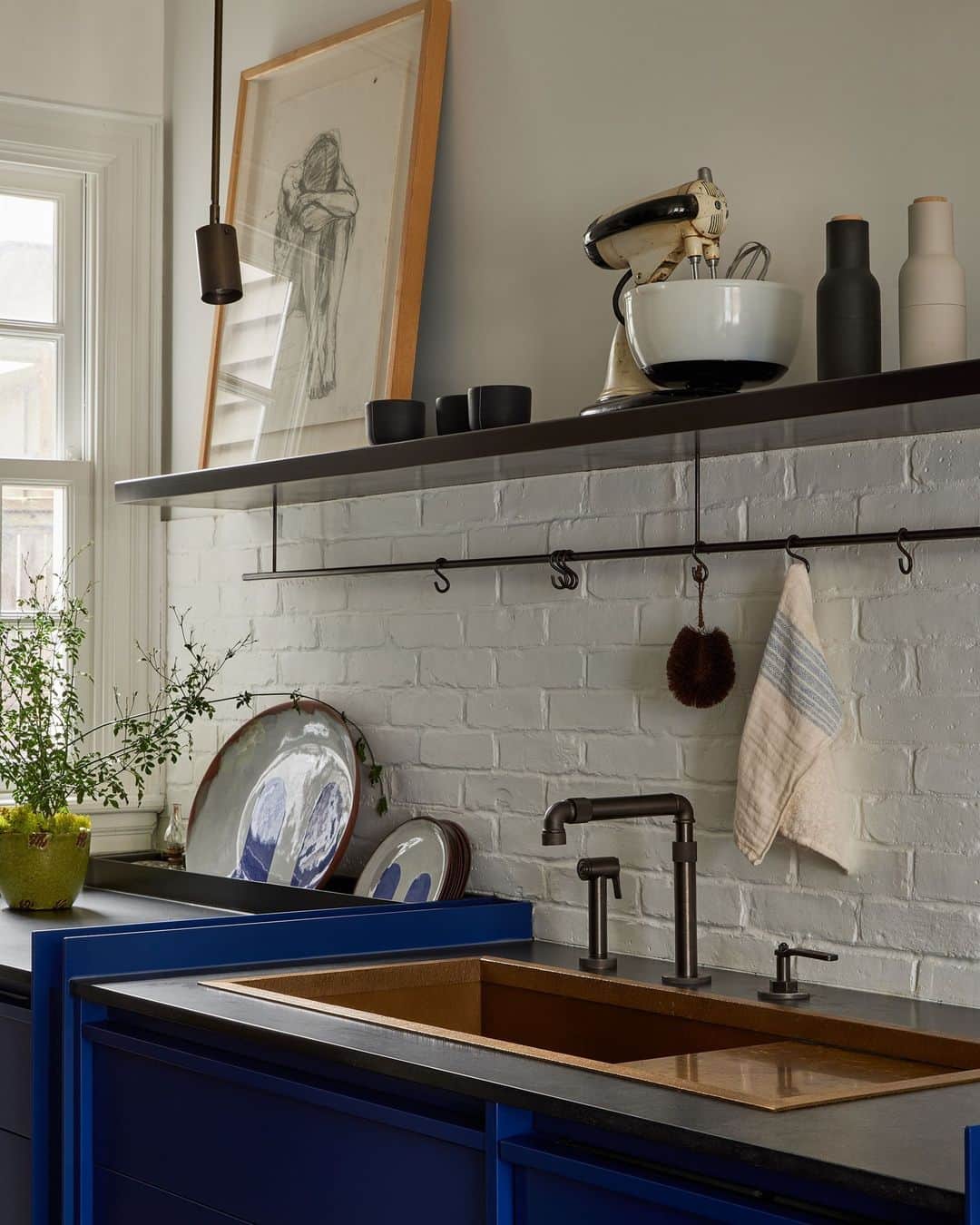 ELLE DECORさんのインスタグラム写真 - (ELLE DECORInstagram)「Having a case of the blues never felt so good. The deep blue hue in this kitchen really takes over, a color choice that marked the finishing touch on an extensive renovation by Toronto designer Sam Sacks (@samsacksdesign). A white brick backsplash covers much of the walls, while an added crown molding looks as if it’s been there since the historic house’s inception. The custom kitchen cabinets, meanwhile, are doused entirely in Sacks’s favored shade, elevating them to sculptural monoliths rather than mere storage. Unexpected nostalgia comes by way of a charcoal drawing of a woman and a vintage Mixmaster lovingly placed on shelves above the kitchen sink—both heirlooms from the client’s grandmother.   To see more blue rooms in this lovely residence, as shown exclusively on elledecor.com, click the link in bio. Written by @cokhio. Photographed by @lomillerphoto.」11月16日 0時01分 - elledecor