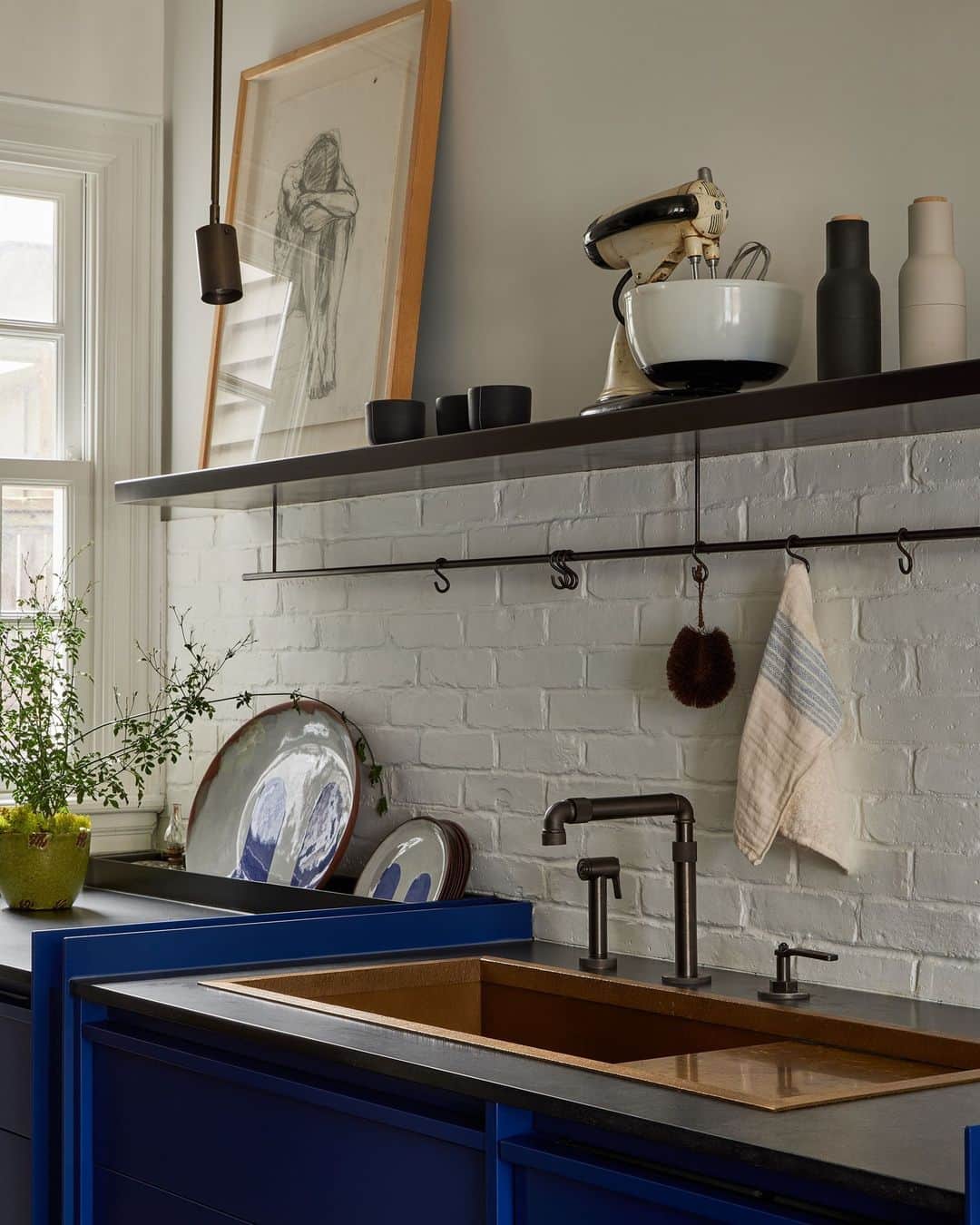 ELLE DECORのインスタグラム：「Having a case of the blues never felt so good. The deep blue hue in this kitchen really takes over, a color choice that marked the finishing touch on an extensive renovation by Toronto designer Sam Sacks (@samsacksdesign). A white brick backsplash covers much of the walls, while an added crown molding looks as if it’s been there since the historic house’s inception. The custom kitchen cabinets, meanwhile, are doused entirely in Sacks’s favored shade, elevating them to sculptural monoliths rather than mere storage. Unexpected nostalgia comes by way of a charcoal drawing of a woman and a vintage Mixmaster lovingly placed on shelves above the kitchen sink—both heirlooms from the client’s grandmother.   To see more blue rooms in this lovely residence, as shown exclusively on elledecor.com, click the link in bio. Written by @cokhio. Photographed by @lomillerphoto.」