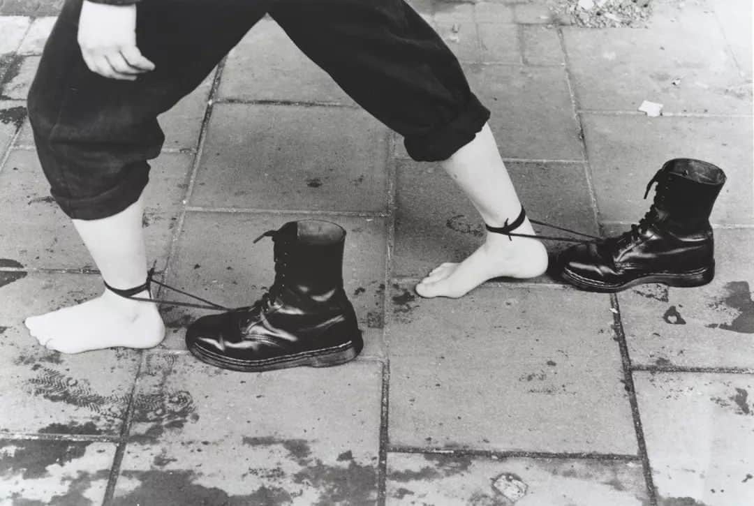 テート・ギャラリーのインスタグラム：「Mona Hatoum first became known in the early 1980s for her series of performance and video pieces which used her own body to explore both the fragility and strength of the human condition under pressure. 🥾 👣  ‘Performance Still’ records one of three street performances which Hatoum carried out in Brixton for the Roadworks exhibition organised in 1985 by the Brixton Artists Collective. The performance had the artist walking barefoot through the streets of Brixton for nearly an hour, with Doc Marten boots, usually worn by both police and skinheads at the time, attached to her ankles by their laces.   Find Hatoum’s artwork in our free Tate Britain display, Modern and Contemporary British Art: No Such Thing as Society: 1980–1990. 🏛️」