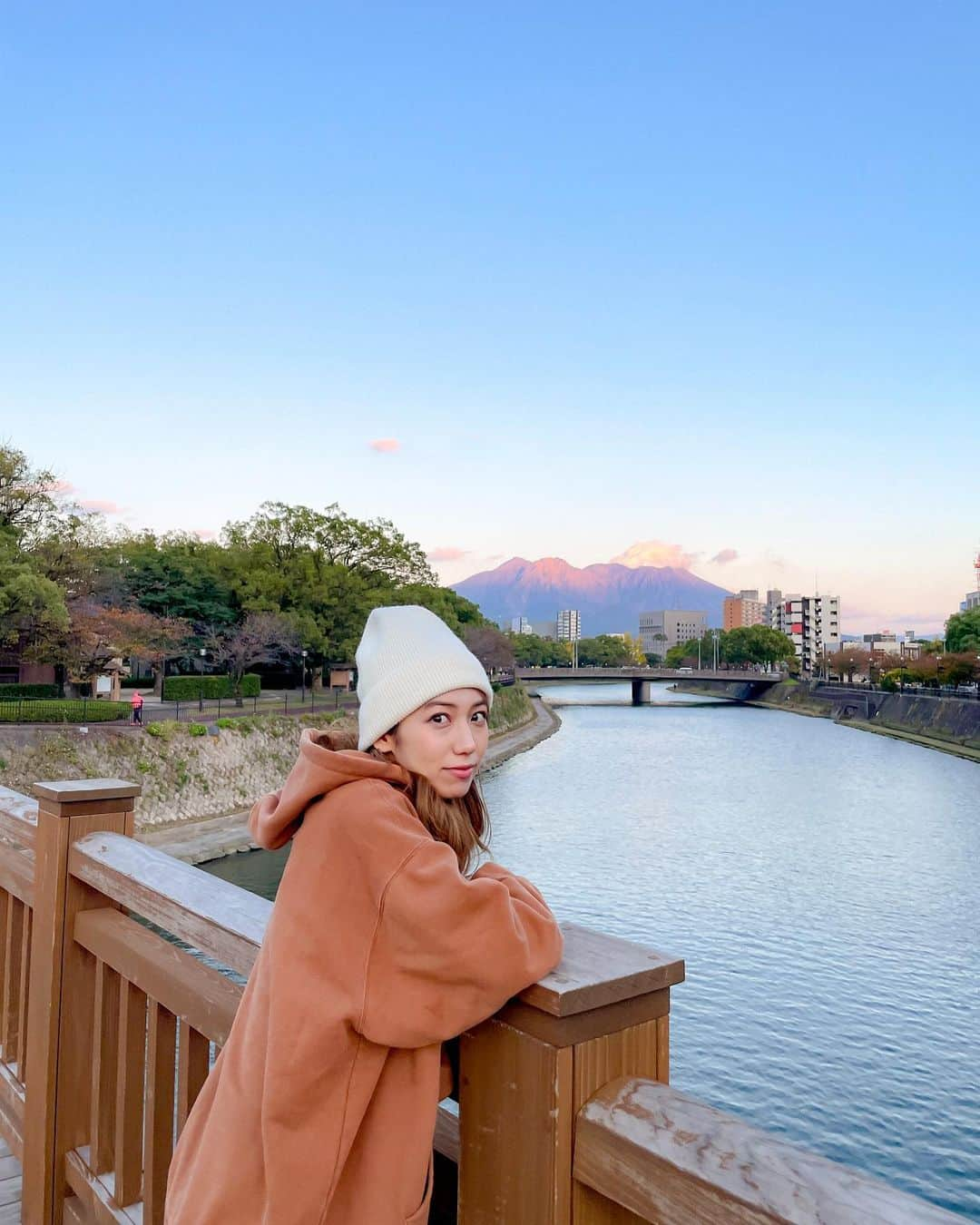 佐藤あいりのインスタグラム：「🍦  大学生時代に歩いていた甲突川沿いの歩道🌳 陽が沈むタイミングで 桜島がほんのりピンクオレンジ🧡  9年前がほんの少し、恋しくなりました。  この日、ちょっとだけ桜島が噴火しました🌋💭 入学1ヶ月後の朝、 起きたら空がどんどん真っ暗になって パチパチパチッと火山灰が空から降ってきて 朝からパニックになった日を思い出しました🙄 そんな日もあったなぁ。  それよりも、ソフトクリームみたいに立った ニット帽が私は気になります。。。😶🍦  #桜島 #鹿児島 #sakurajima #kagoshima」