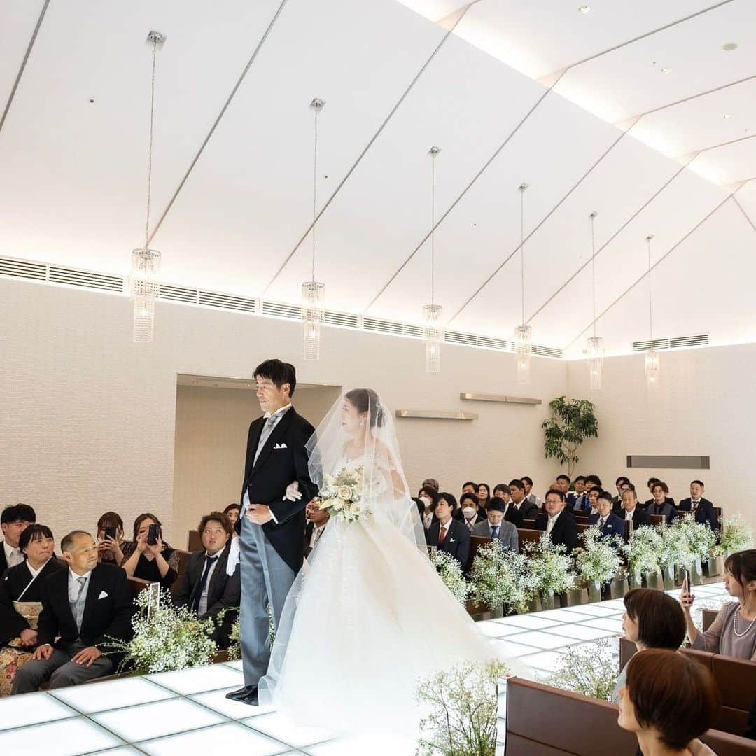 【公式】アルカンシエルリュクスマリアージュ名古屋のインスタグラム：「【挙式レポート⛪️💍】  白亜のチャペルでの挙式は、美しい光に満ちています✨  『花嫁様の人生』を表すバージンロード。 その人生の輝きが、新郎様と共に永遠に続くことを願い、明るくライトアップします👰‍♀️🌟 そして、大切な方のエスコートのもと、一歩ずつ、これまでの人生を思い出しながら祭壇まで進まれます😌  また、ジャケットセレモニーやベールダウンの儀式を通して、親御様からの「幸せになってね」と、温かいメッセージが💓  ゲストの皆様からの祝福の拍手が優しく響く中、愛を誓われたおふたり。 この度は誠におめでとうございます♪ どうぞ末永くお幸せに…🕊️  💒名駅徒歩5分の結婚式場  『#感謝を式のまんなかに。』をテーマに、青空を貸切る祝福のステージと上質な空間で生まれる、ゲストとの忘れられない一日のつくりかたを紹介しています💓  👇🏻をタップ🌈👣 @arcenciel.luxenagoya  2023年度版　JapanBrandCollectionに掲載されました 公式アカウント⇨ @japanbrandcollection lit.link/japanbrandcollection  #アルカンシエル #アルカンシエルluxemariage名古屋 #アルカンシエルリュクスマリアージュ名古屋 #アルカン花嫁 #名古屋花嫁 #名古屋プレ花嫁 #名古屋ウエディング #名古屋ウェディング #名古屋結婚式 #愛知花嫁 #日本中のプレ花嫁さんと繋がりたい #結婚式レポ #結婚式レポート #ウエディングレポート #ウェディングレポート #ウェディングレポ #ウエディングレポ #2023秋婚 #2023冬婚 #2024春婚 #2024夏婚 #2024秋婚 #チャペル #チャペルウェディング #挙式レポ #ベールダウン #ジャケットセレモニー #新婦入場 #新郎入場」